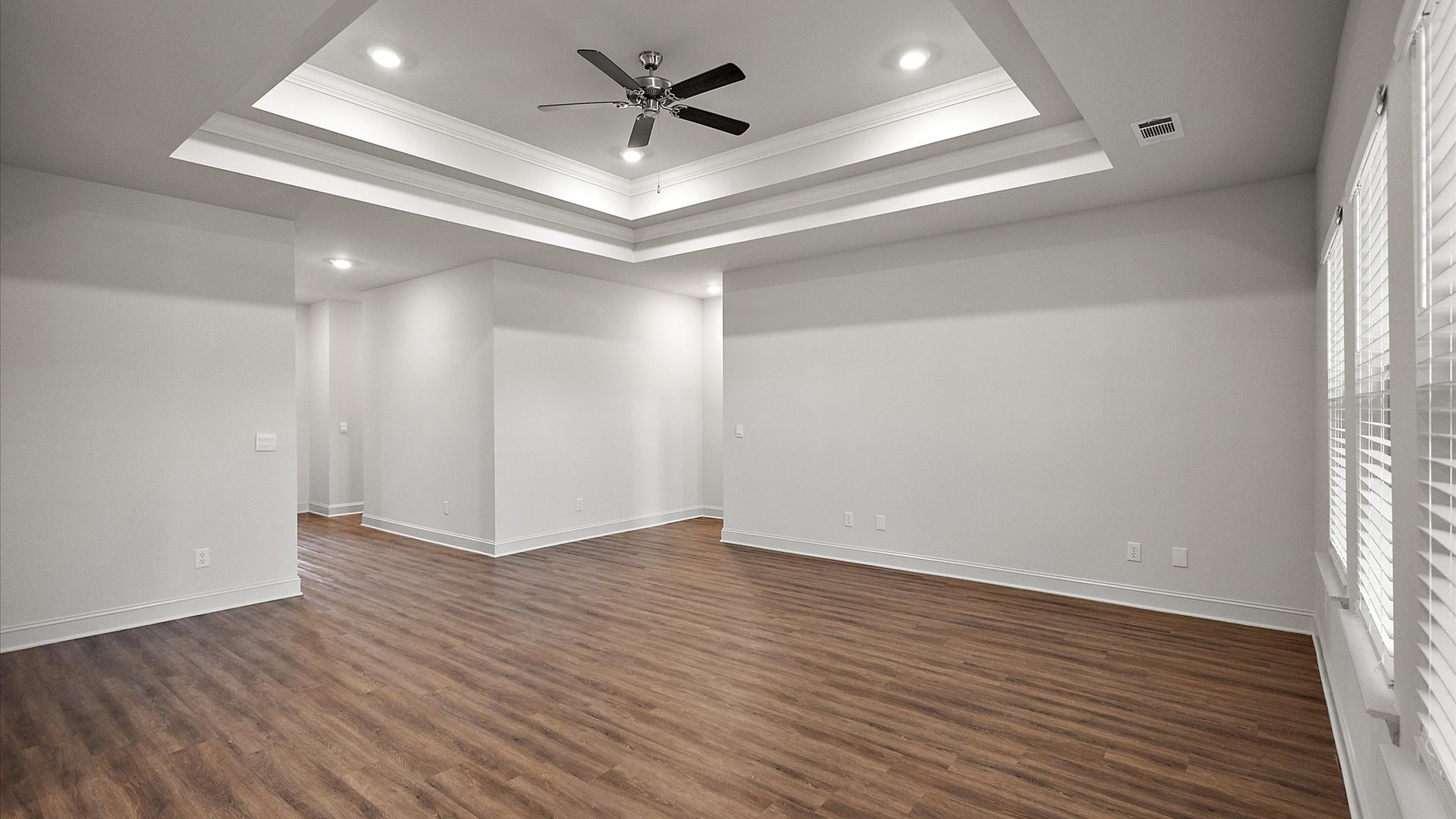 Modern open concept living room with hardwood floors, tray ceilings, ceiling fan, and large windows.