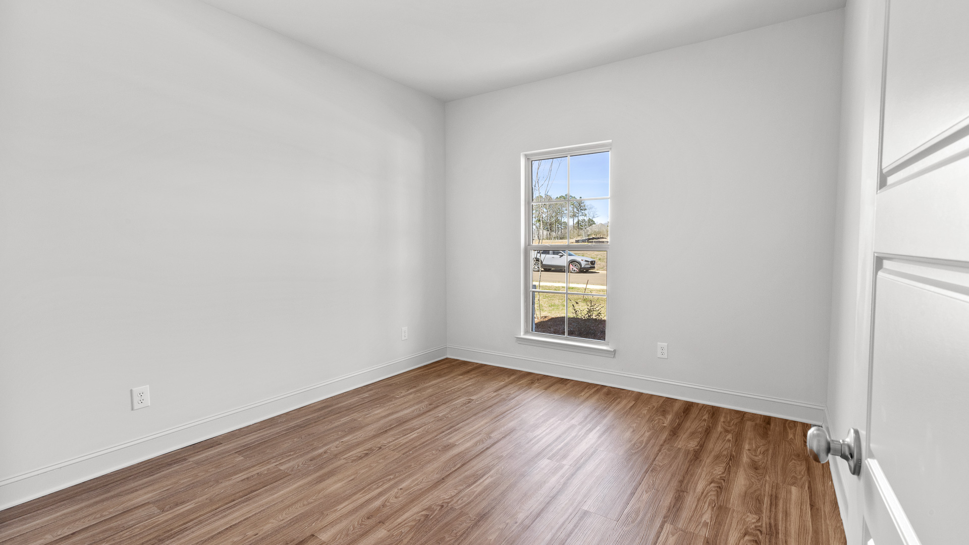 Another bedroom with hardwood floors and large single windows for natural light.