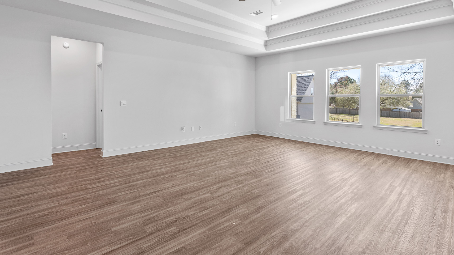 A spacious open floor plan living room, large windows, hardwood floors, and trey ceilings.