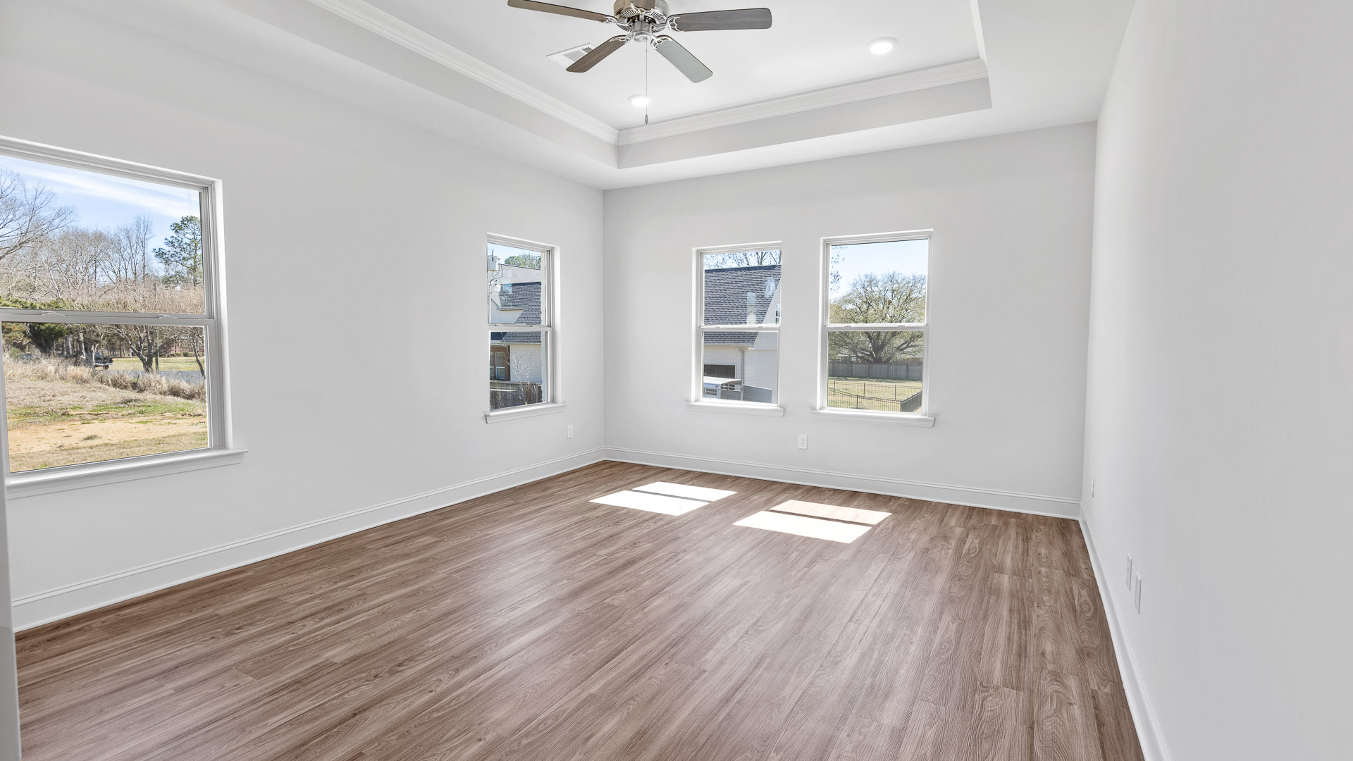 Primary bedroom with hardwood floors, large windows, and trey ceilings.