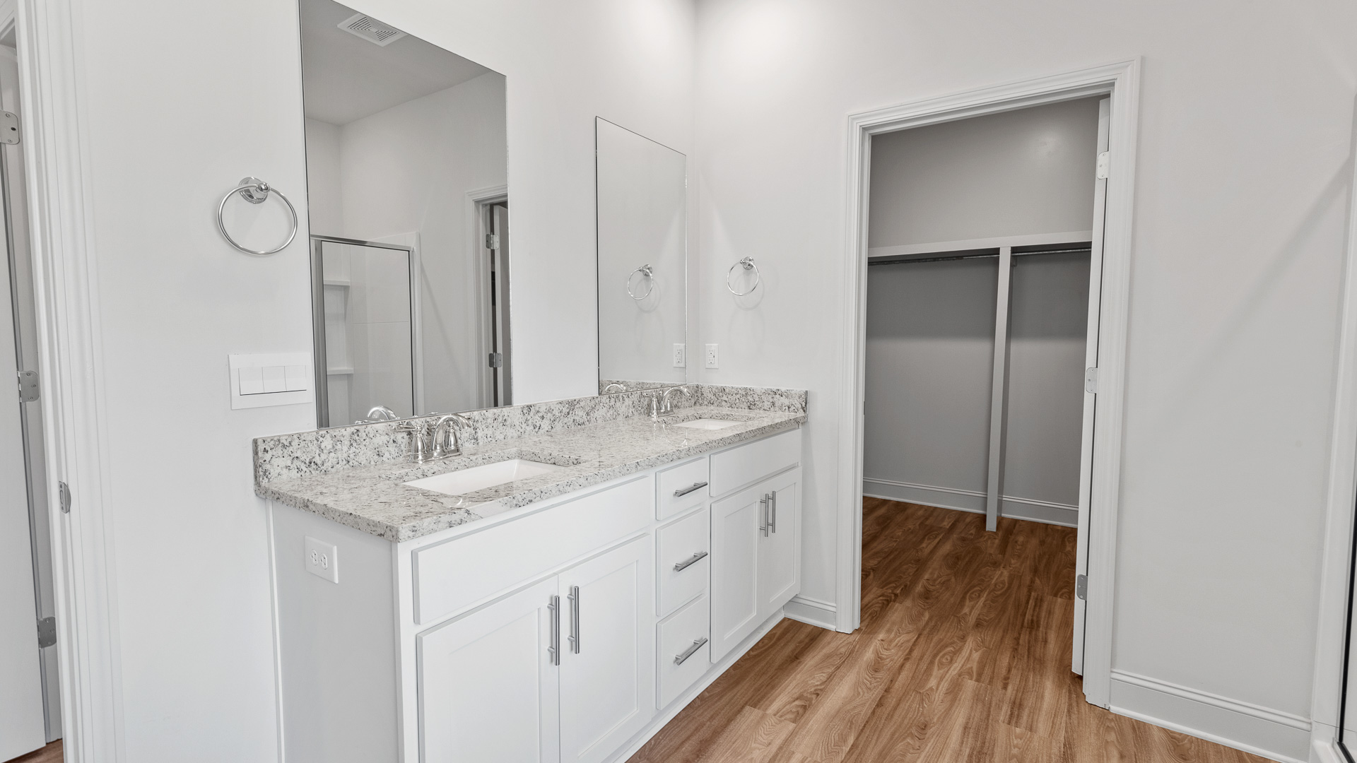 A modern bathroom featuring a double sink vanity with light gray granite countertops and walkin shower and adjacent garden tub., bright light fixtures, and closet in the space.