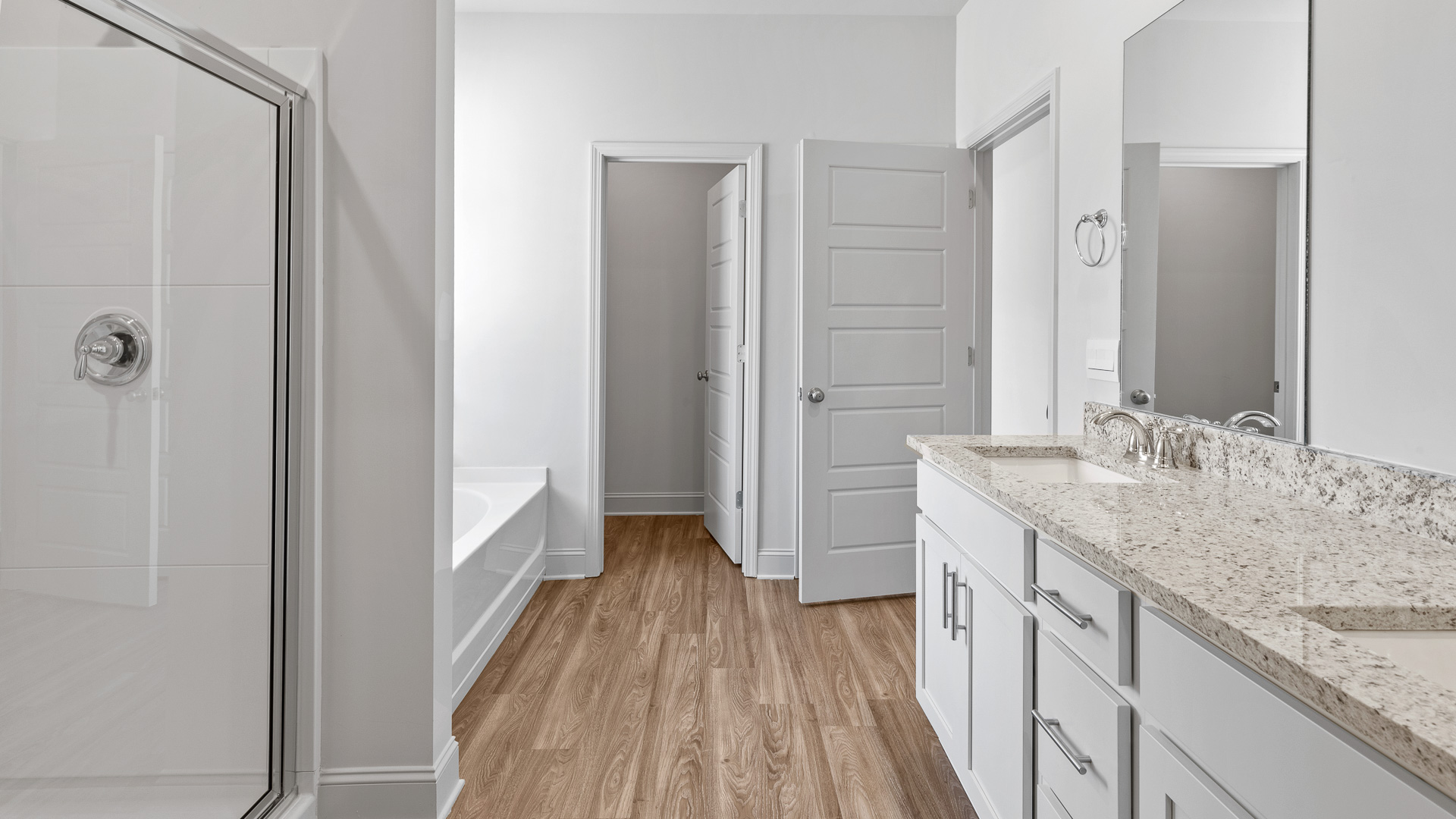 A modern bathroom featuring a double sink vanity with light gray granite countertops and walkin shower and adjacent garden tub., bright light fixtures, and closet in the space.