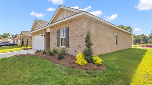 Other side exterior single story home with multi color brown brick and white paneling and brown shutters on the windows with side walk to the front door. The two-car garage and driveway.