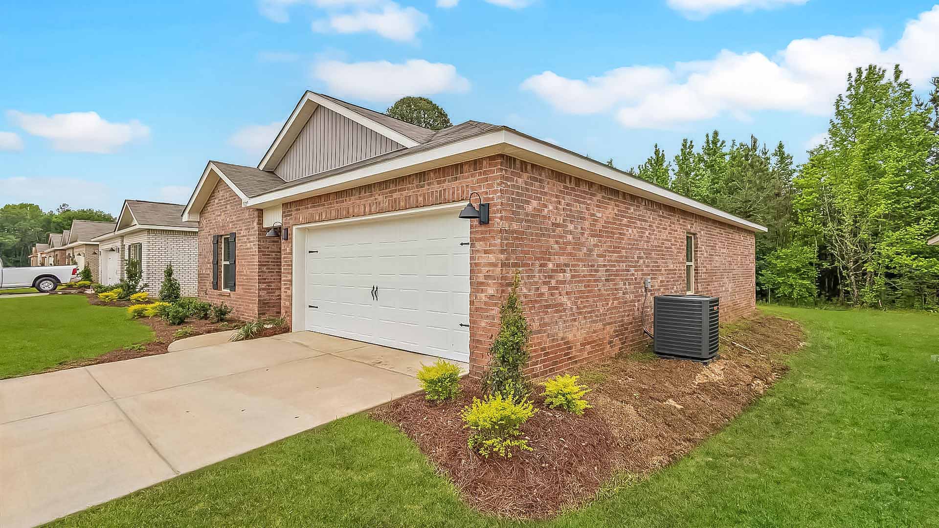 Other side exterior single story home with red/brown brick and white paneling and black shutters on the windows with side walk to the front door. The two-car garage and driveway.