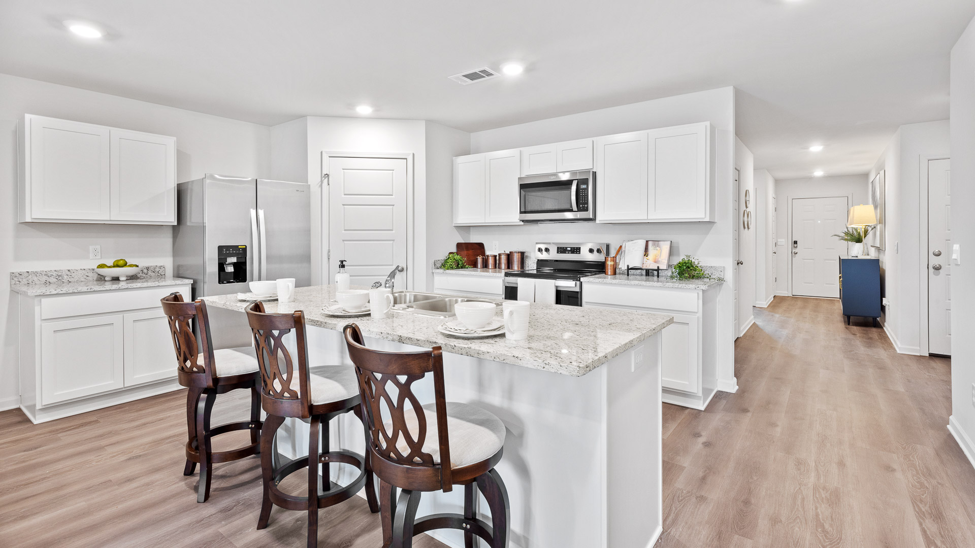 Kitchen has granite countertops, white shaker-style cabinets, an island with a sink, and stainless steel appliances.