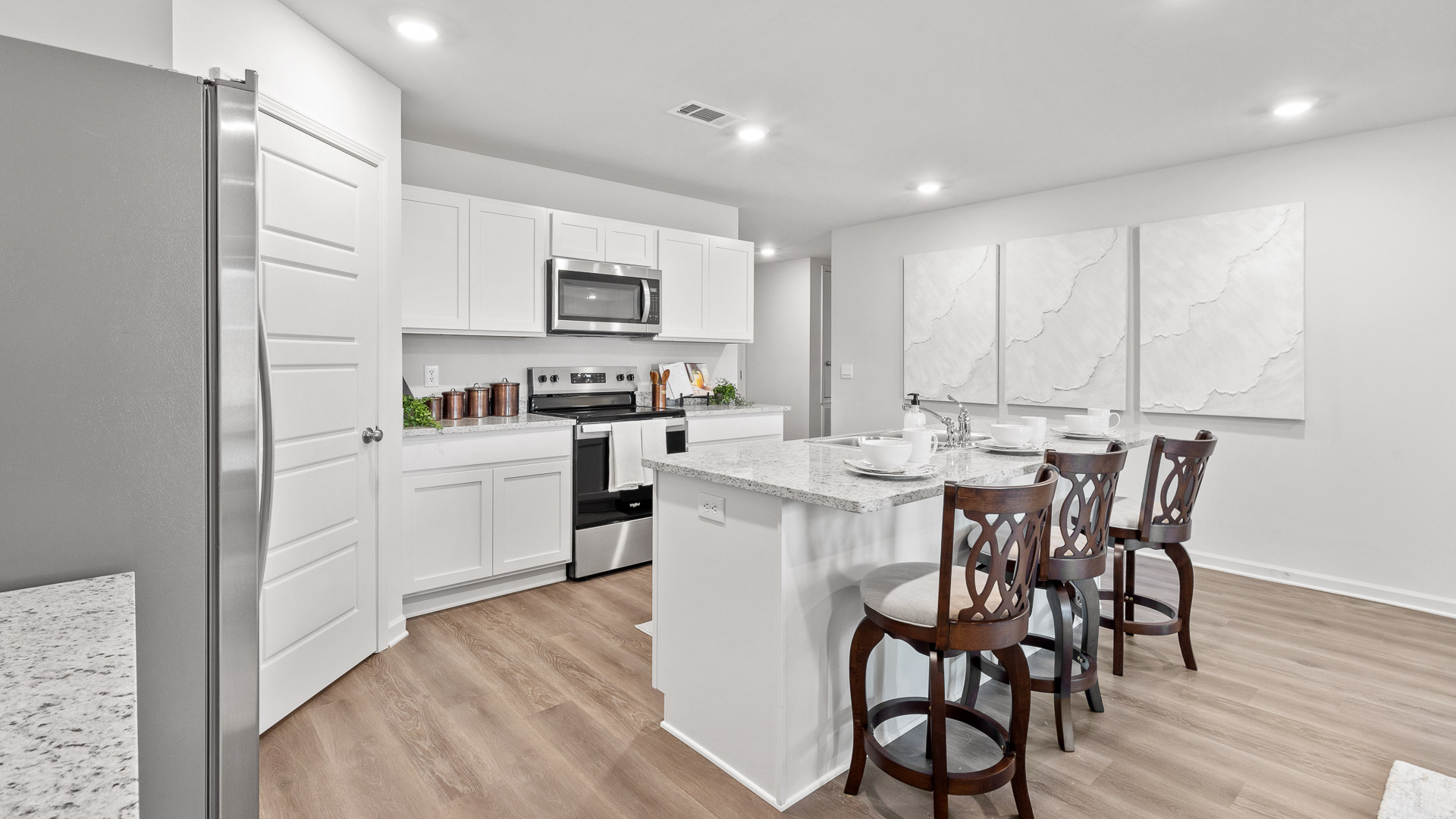 Kitchen has granite countertops, white shaker-style cabinets, an island with a sink, and stainless steel appliances.