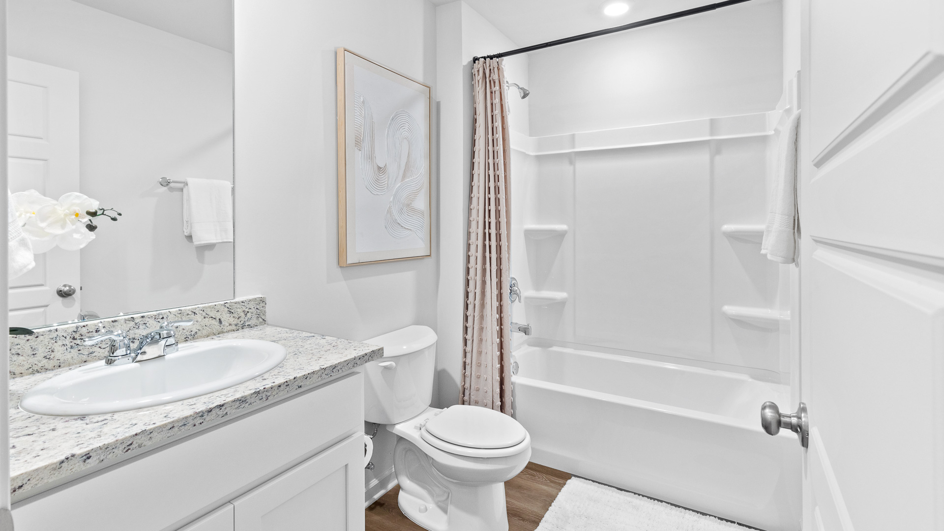 Full bath in between bedrooms 2 and 3 with granite countertops, white shaker-style cabinets and a white shower with a tub.