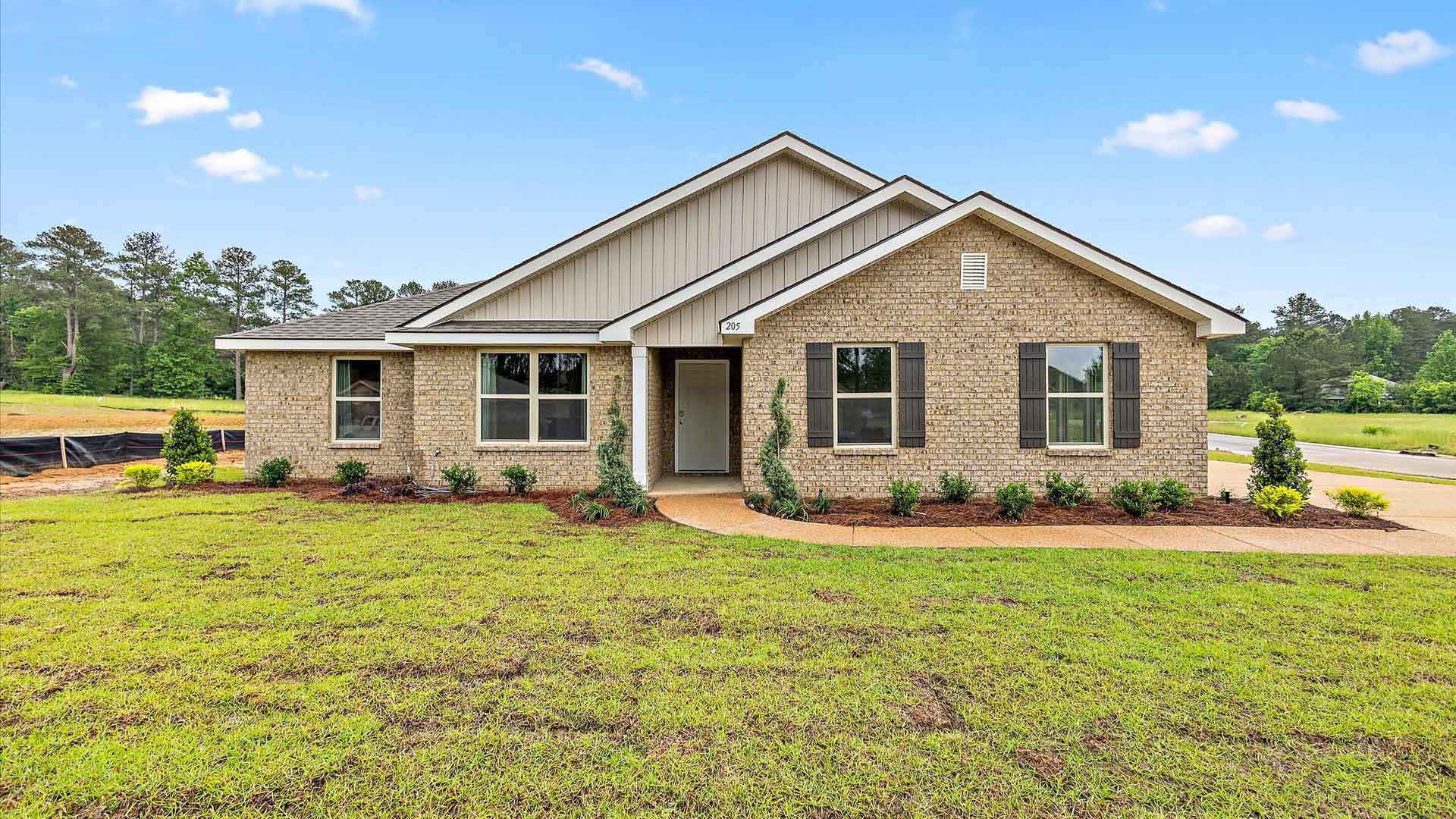 Front exterior single story home with tan brick, white paneling, and black shutters on the windows with front entry and covered porch. The two-car garage and driveway are on the side of the house.