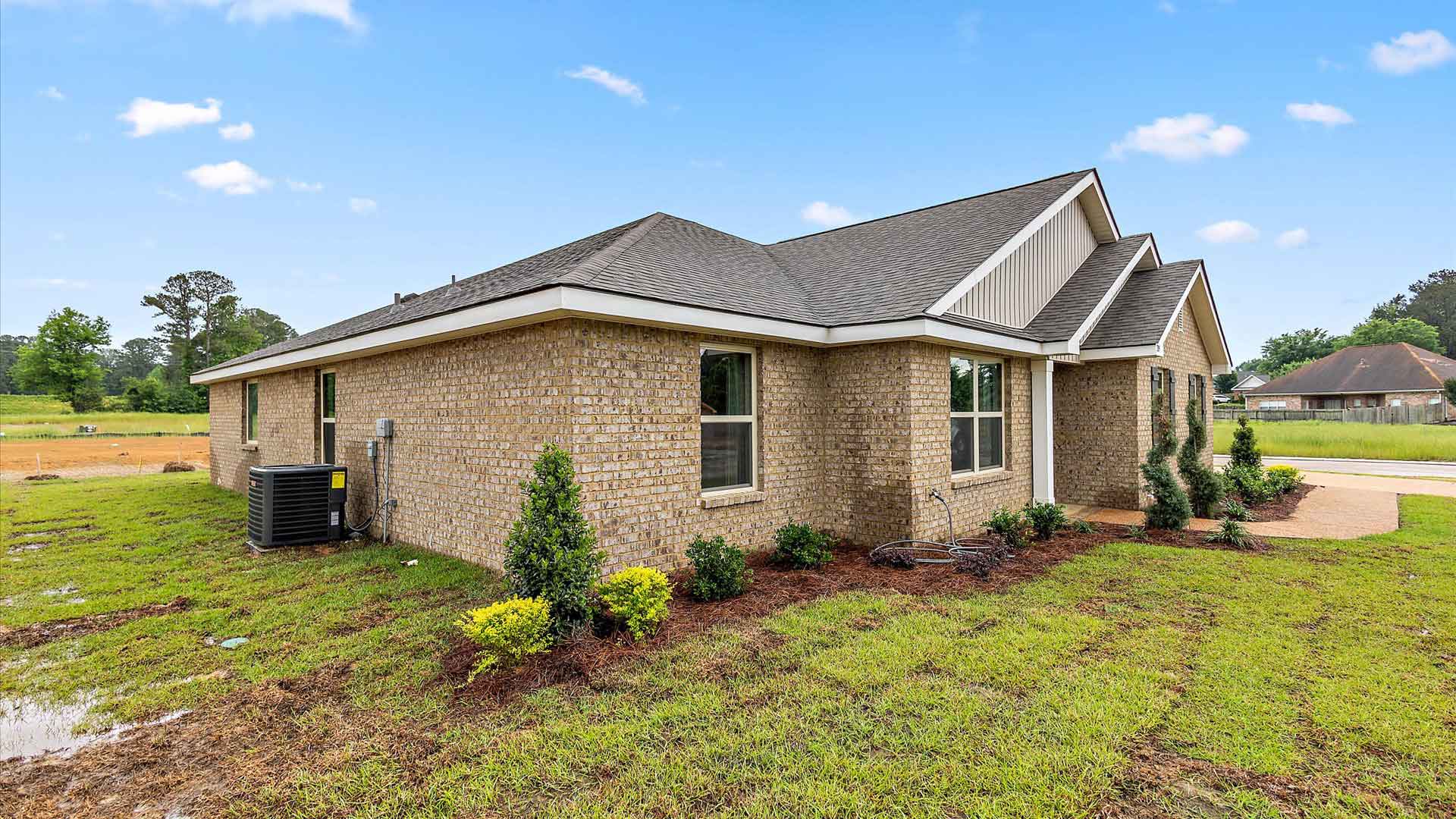 Side exterior single story home with tan brick and white paneling with several windows.