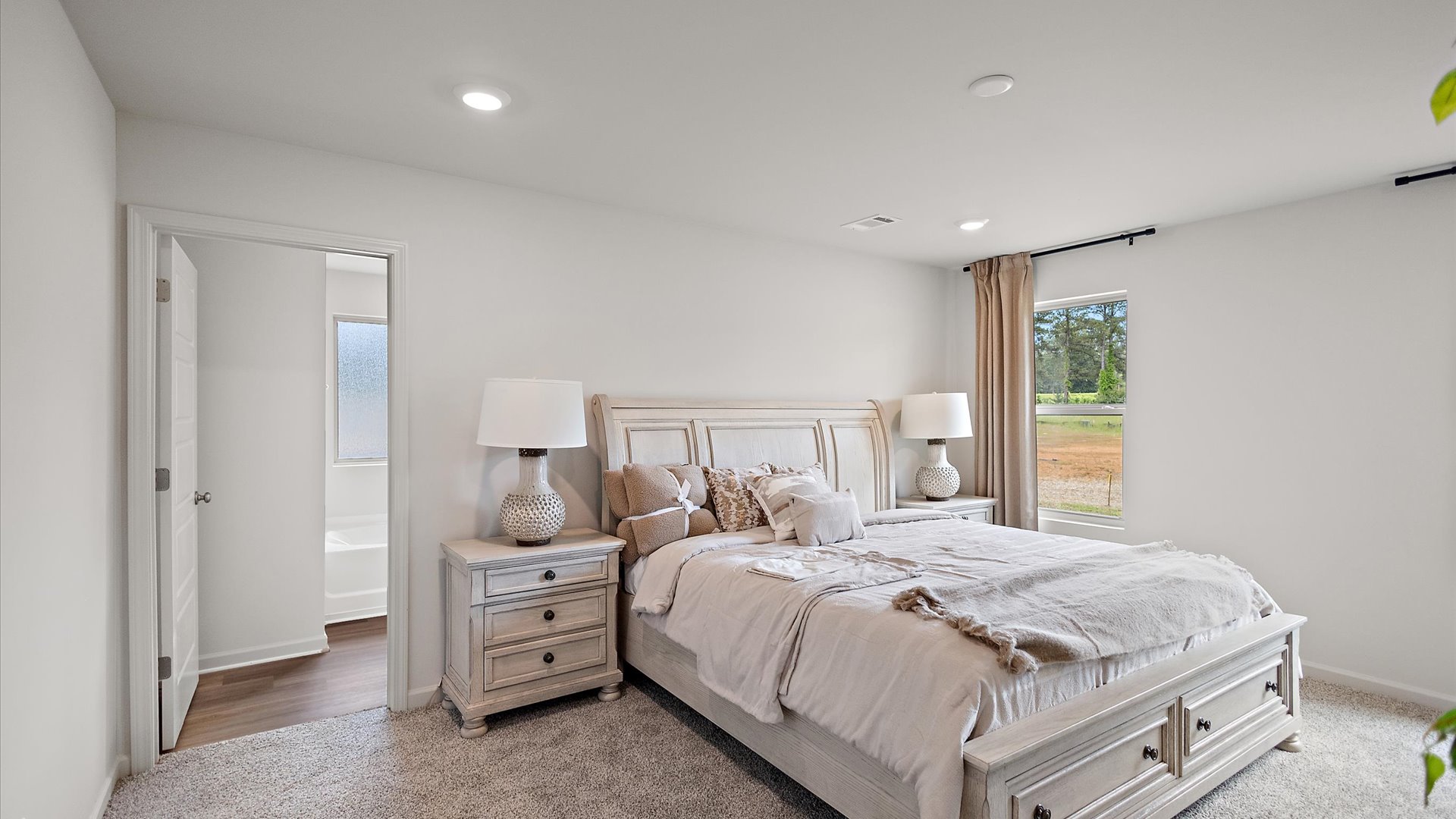 Primary bedroom with carpeted floors, large windows, and the primary bathroom door.
