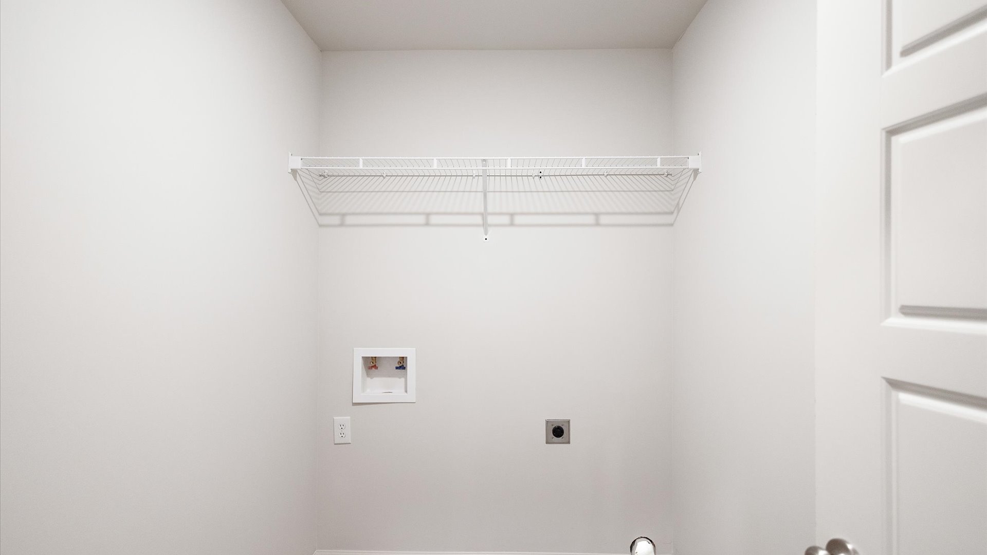 Laundry area has room for a washer and dryer with mounted wire shelving.