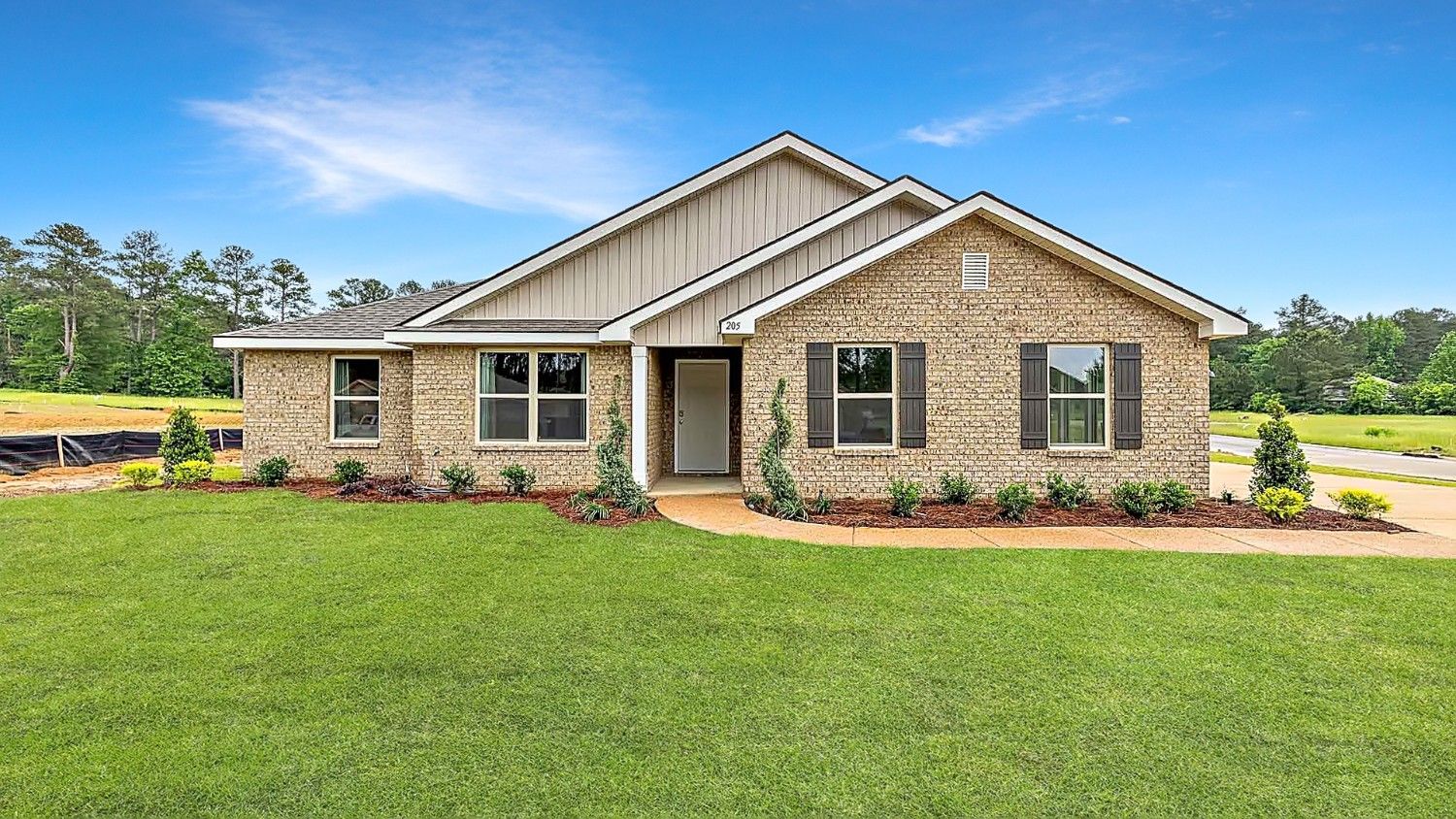 Front exterior single story home with tan brick, white paneling, and black shutters on the windows with front entry and covered porch. The two-car garage and driveway are on the side of the house.