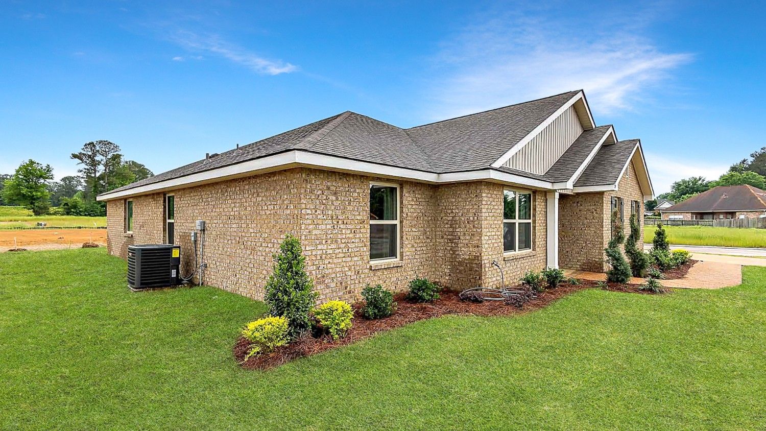 Front exterior single story home with tan brick, white paneling, and black shutters on the windows with front entry and covered porch. The two-car garage and driveway are on the side of the house.