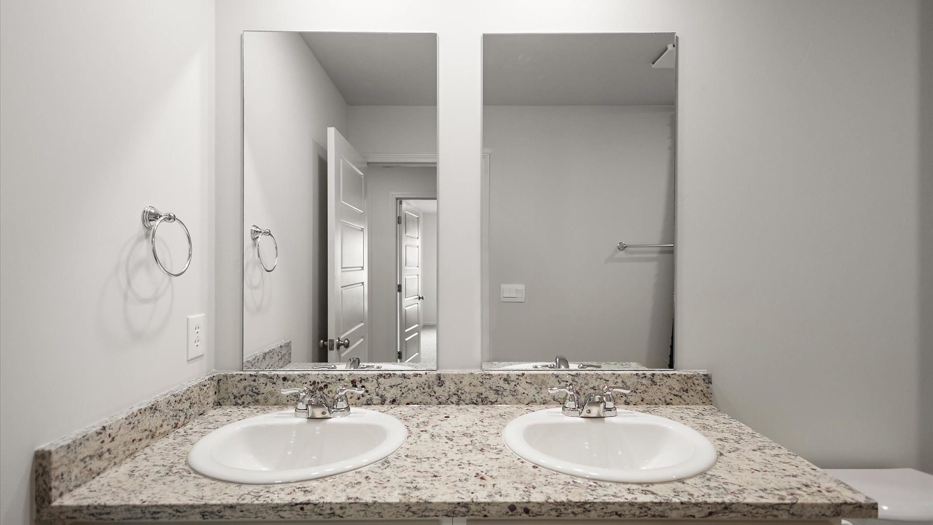 A modern bathroom featuring a double vanity with granite countertops, bright light fixtures, and closet in the space.