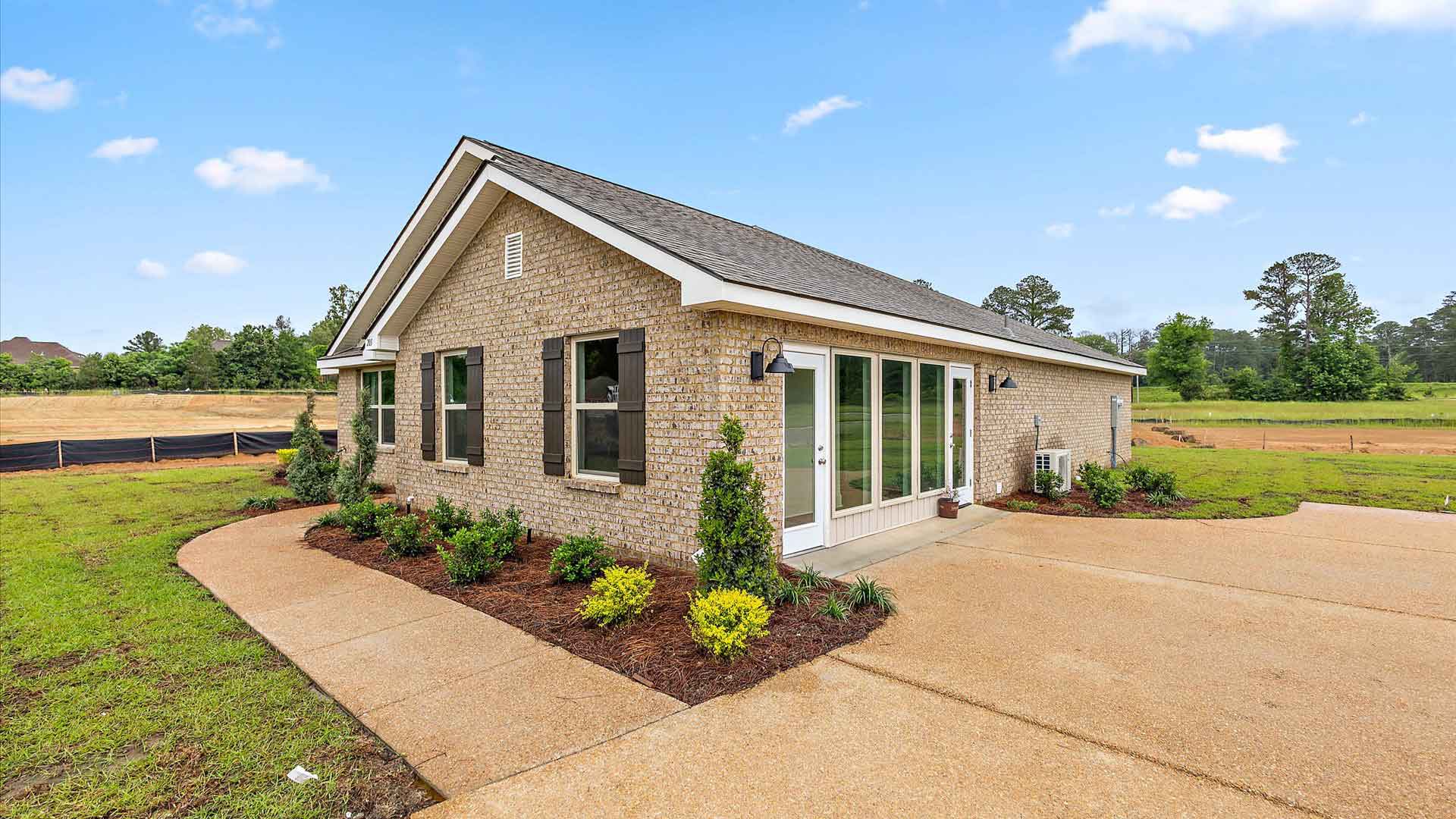 Other side exterior single story home with tan brick and white paneling and black shutters on the windows with side walk to the front door. The two-car garage and driveway are in view.