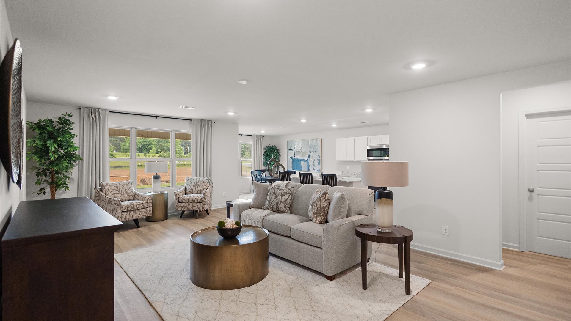 A spacious open floor plan living room, large windows, hardwood floors, and trey ceilings.