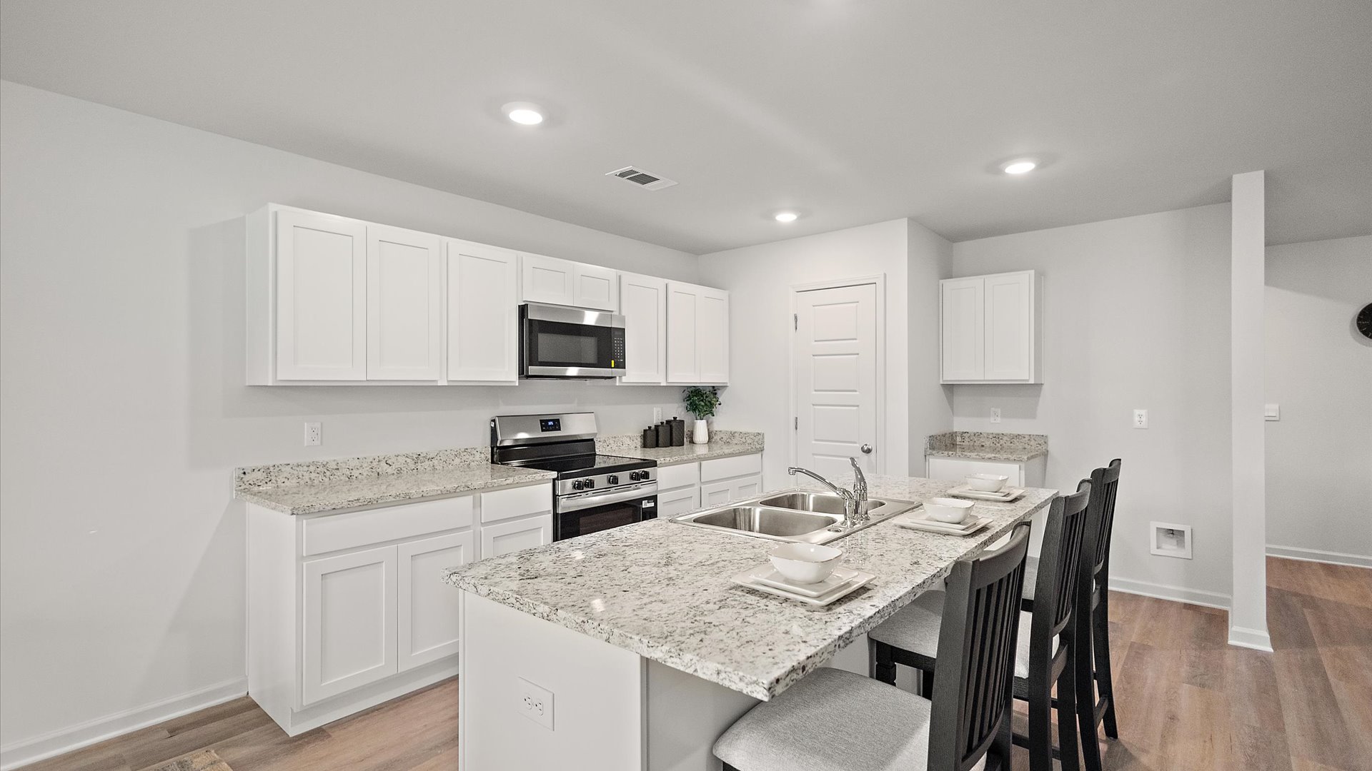 Spacious kitchen with granite countertops, large island, white cabinets, and stainless steel appliances with pantry in the corner.