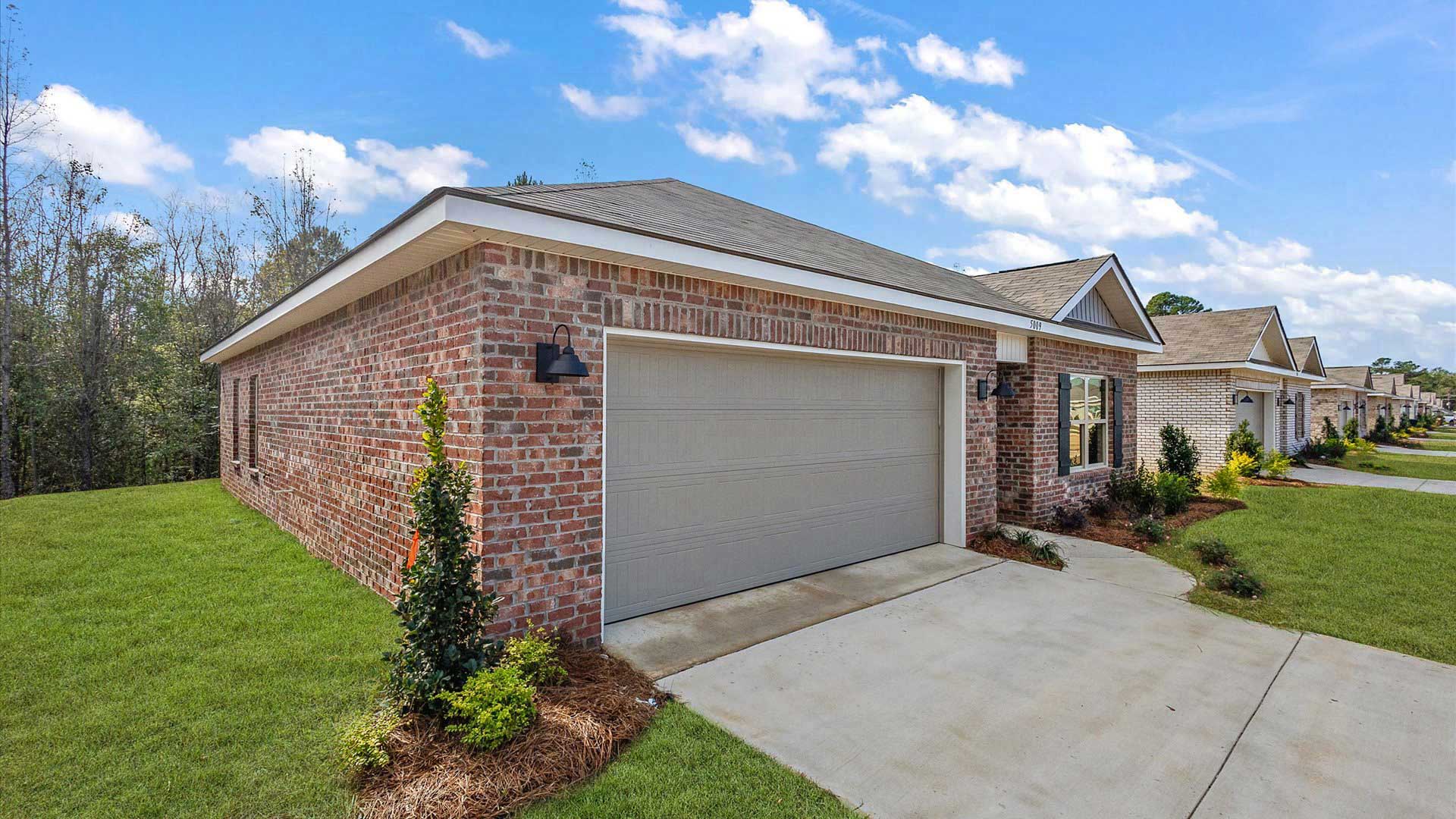 Side exterior single story home with multi color brown brick and white paneling and brown shutters on the windows with side walk to the front door. The two-car garage and driveway.