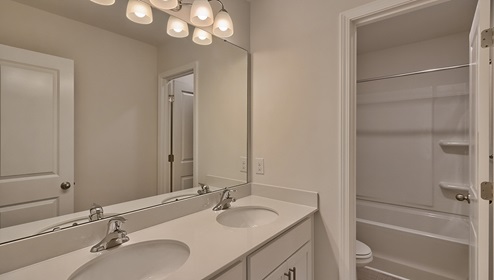 Bathroom with double sinks, white counters and cabinets, bathtub and toilet in closed area