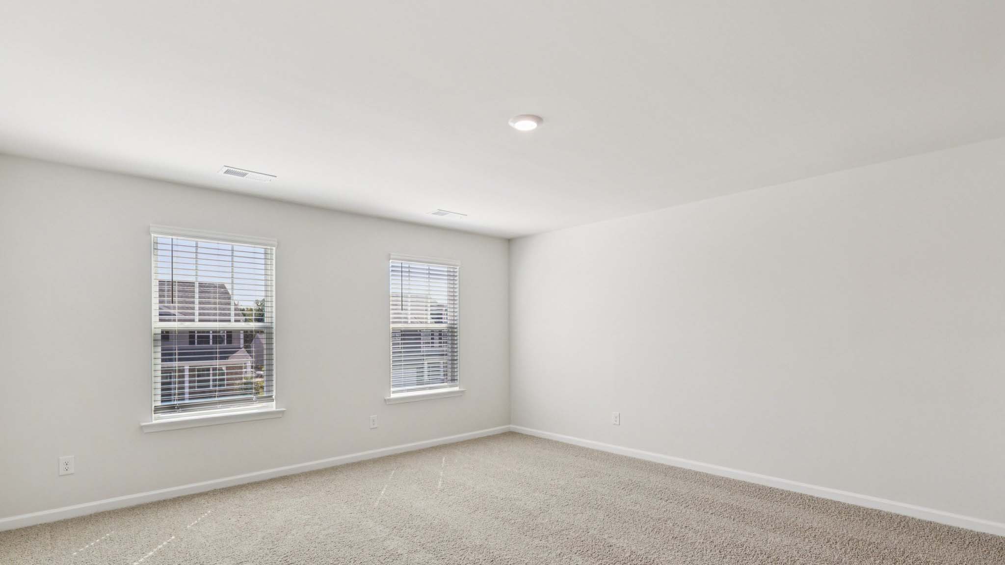 Primary carpeted bedroom with two large windows