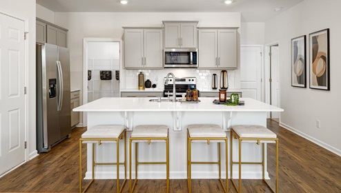 Kitchen and island with grey cabinets, white countertops, white subway tile backsplash, breakfast bar area and stainless steel appliances. New Home in Charlotte, North Carolina