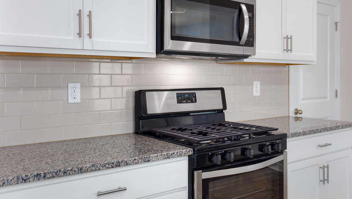 Kitchen and island with white cabinets, white subway tile backsplash and stainless steel appliances