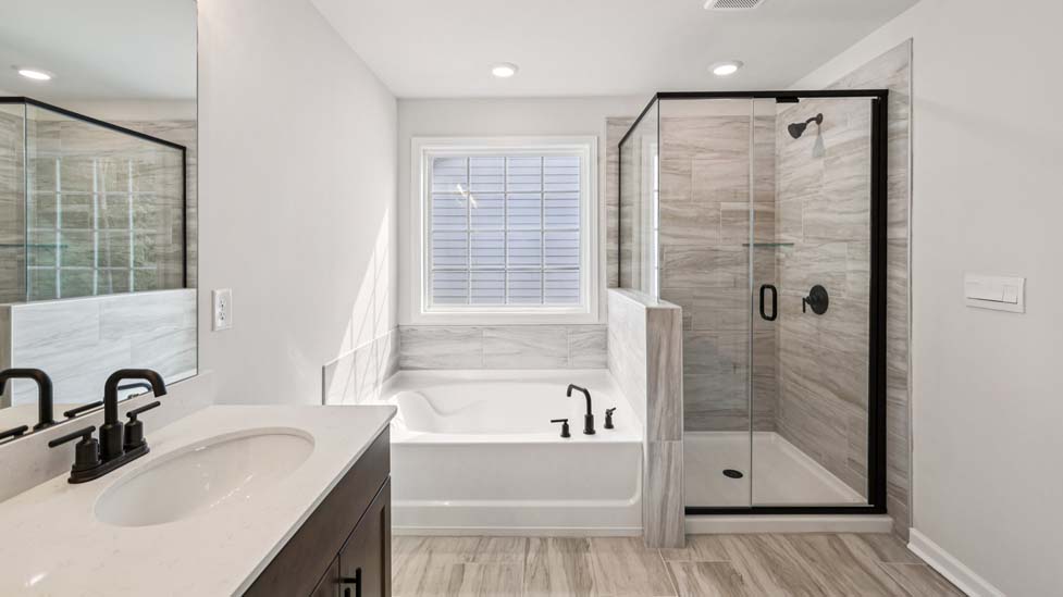 Primary bathroom with double sinks, brown cabinets and bathtub and glass door shower combination