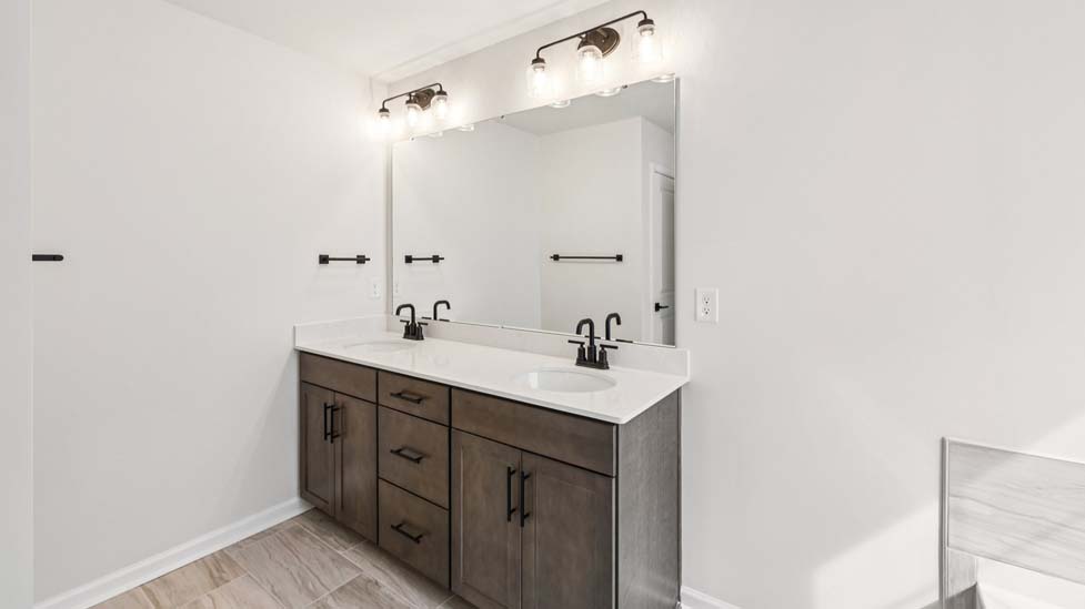 Primary bathroom with double sinks, brown cabinets and bathtub and glass door shower combination