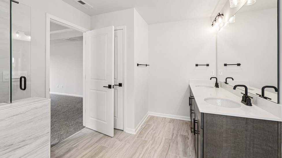 Primary bathroom with double sinks, brown cabinets and bathtub and glass door shower combination