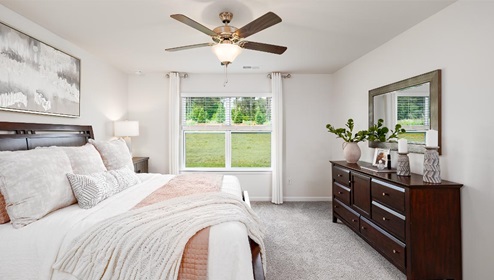 Carpeted primary bedroom with large window and ceiling fan