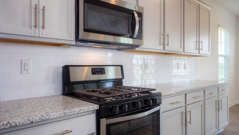 Kitchen and island with grey cabinets, white subway tile backsplash, and stainless steel appliances