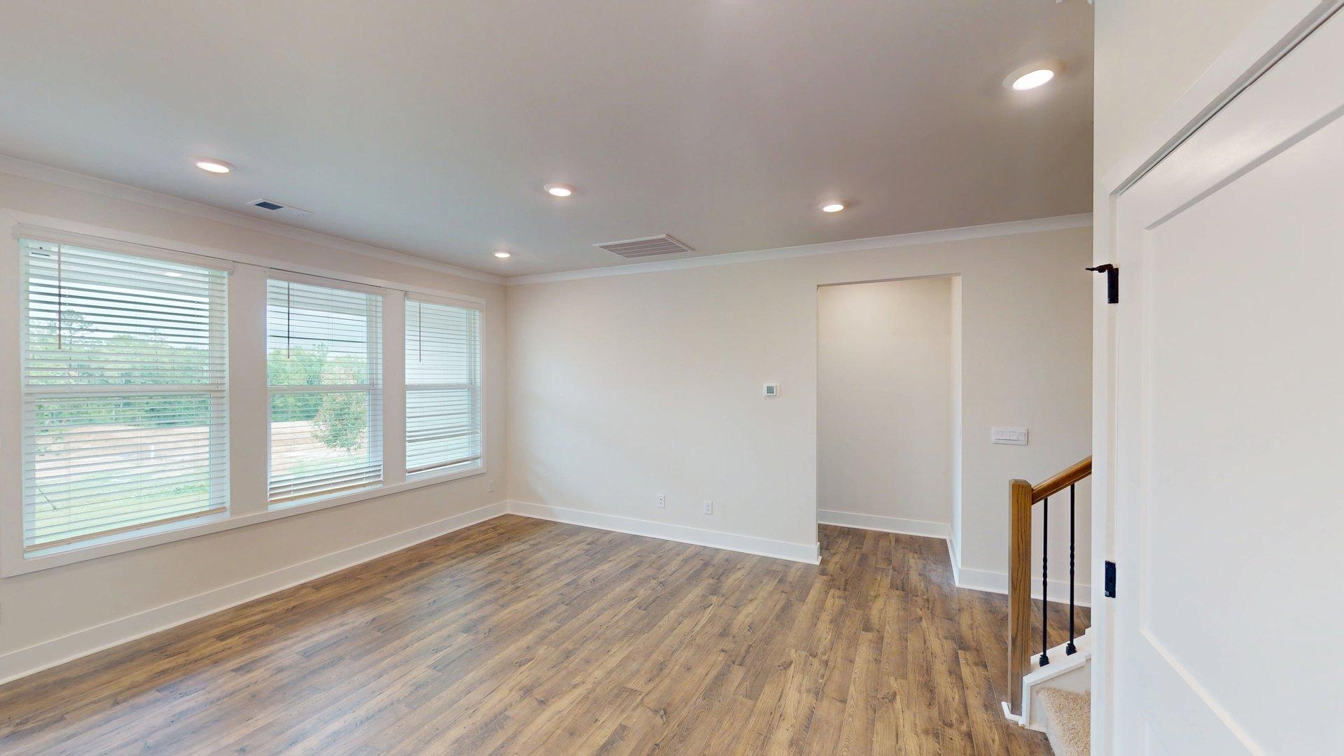 Open concept living room beside ktichen with large windows and staircase