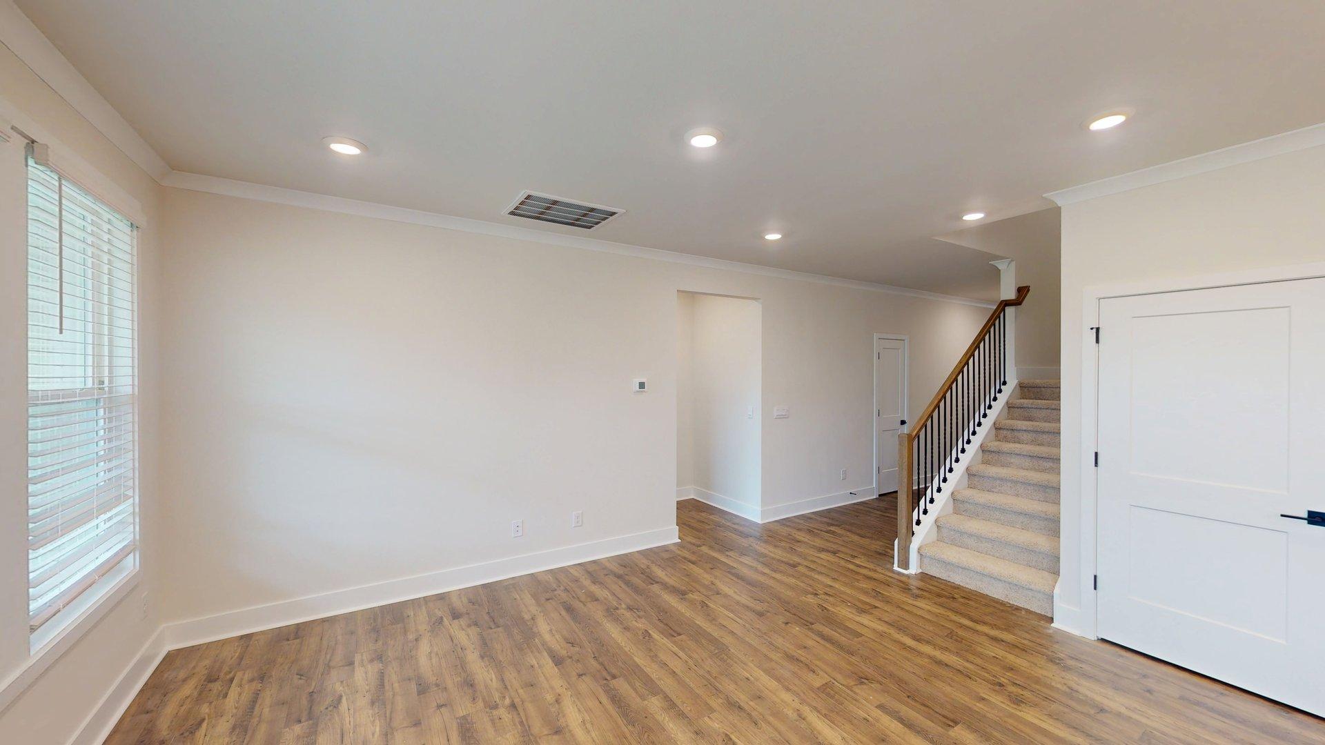 Open concept living room beside ktichen with large windows and staircase