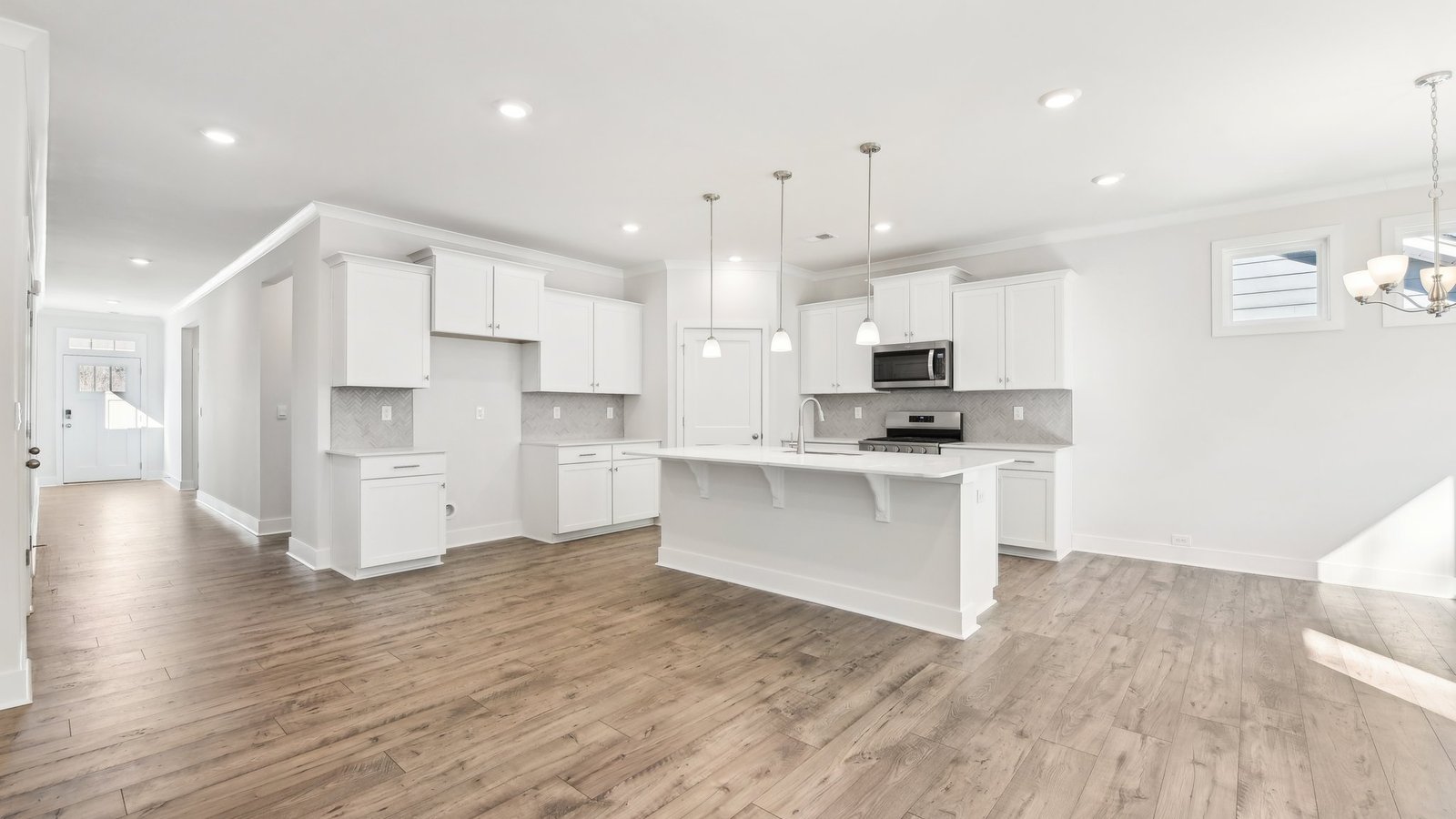 Kitchen and island with white cabinets, tile backsplash, quartz countertops, and stainless steel appliances