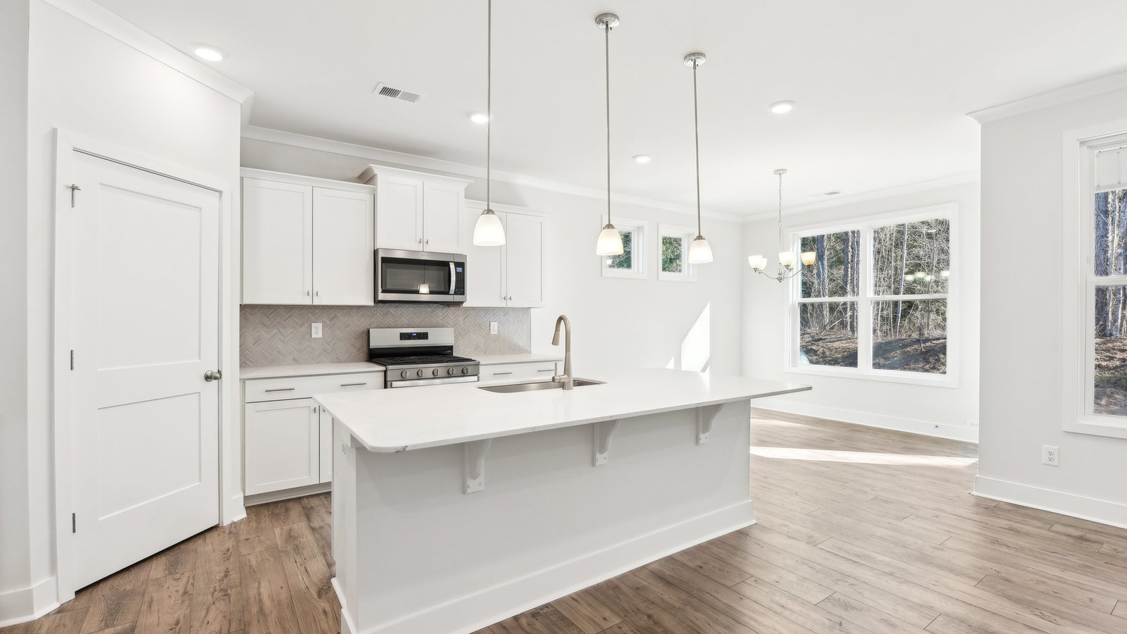 Kitchen and island with white cabinets, tile backsplash, quartz countertops, and stainless steel appliances