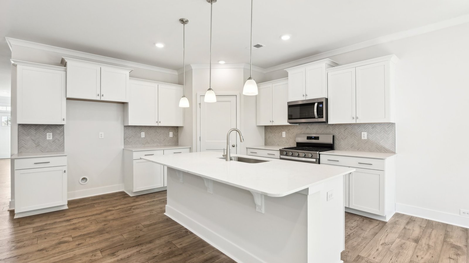 Kitchen and island with white cabinets, tile backsplash, quartz countertops, and stainless steel appliances