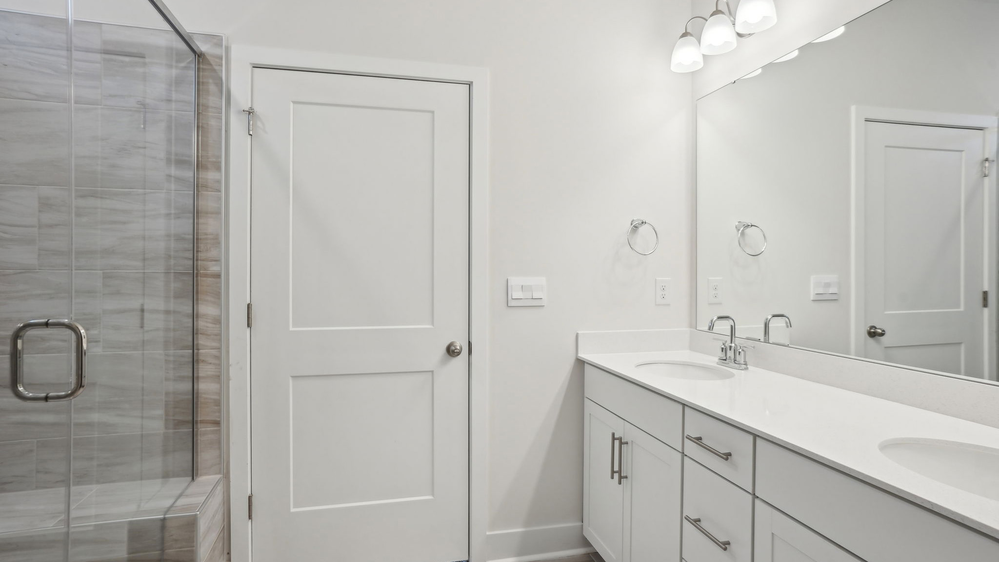 Primary bathroom  with double sink vanity, white counters and cabinets, and standing glass door shower
