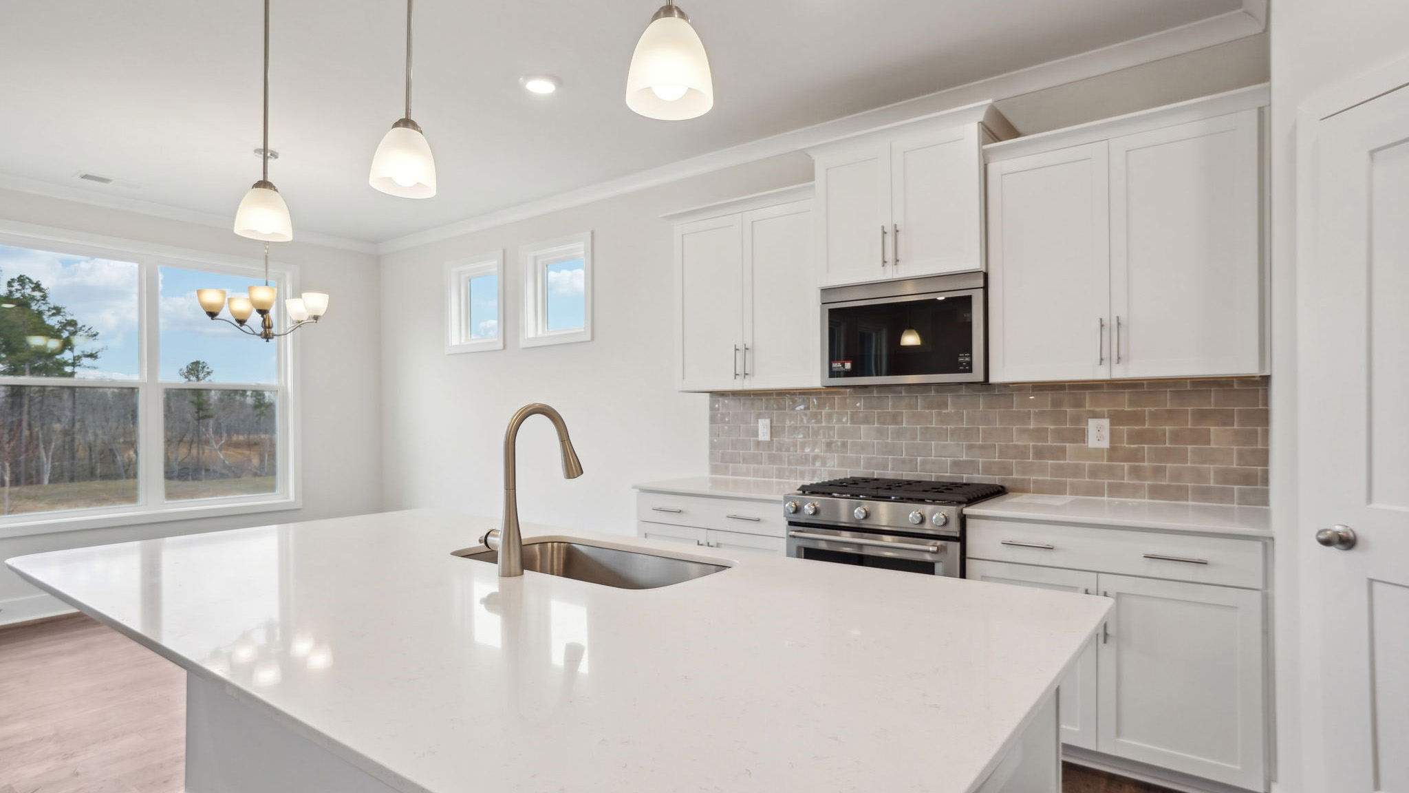 Kitchen and island with white cabinets, tile backsplash, quartz countertops, and stainless steel appliances