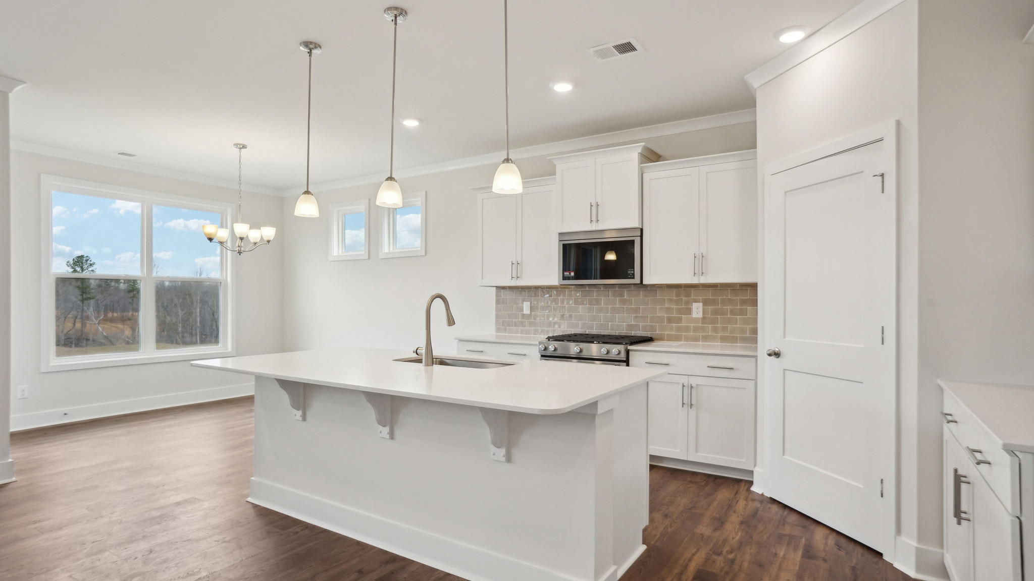 Kitchen and island with white cabinets, tile backsplash, quartz countertops, and stainless steel appliances