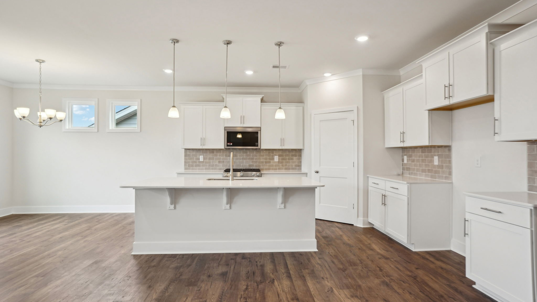 Kitchen and island with white cabinets, tile backsplash, quartz countertops, and stainless steel appliances