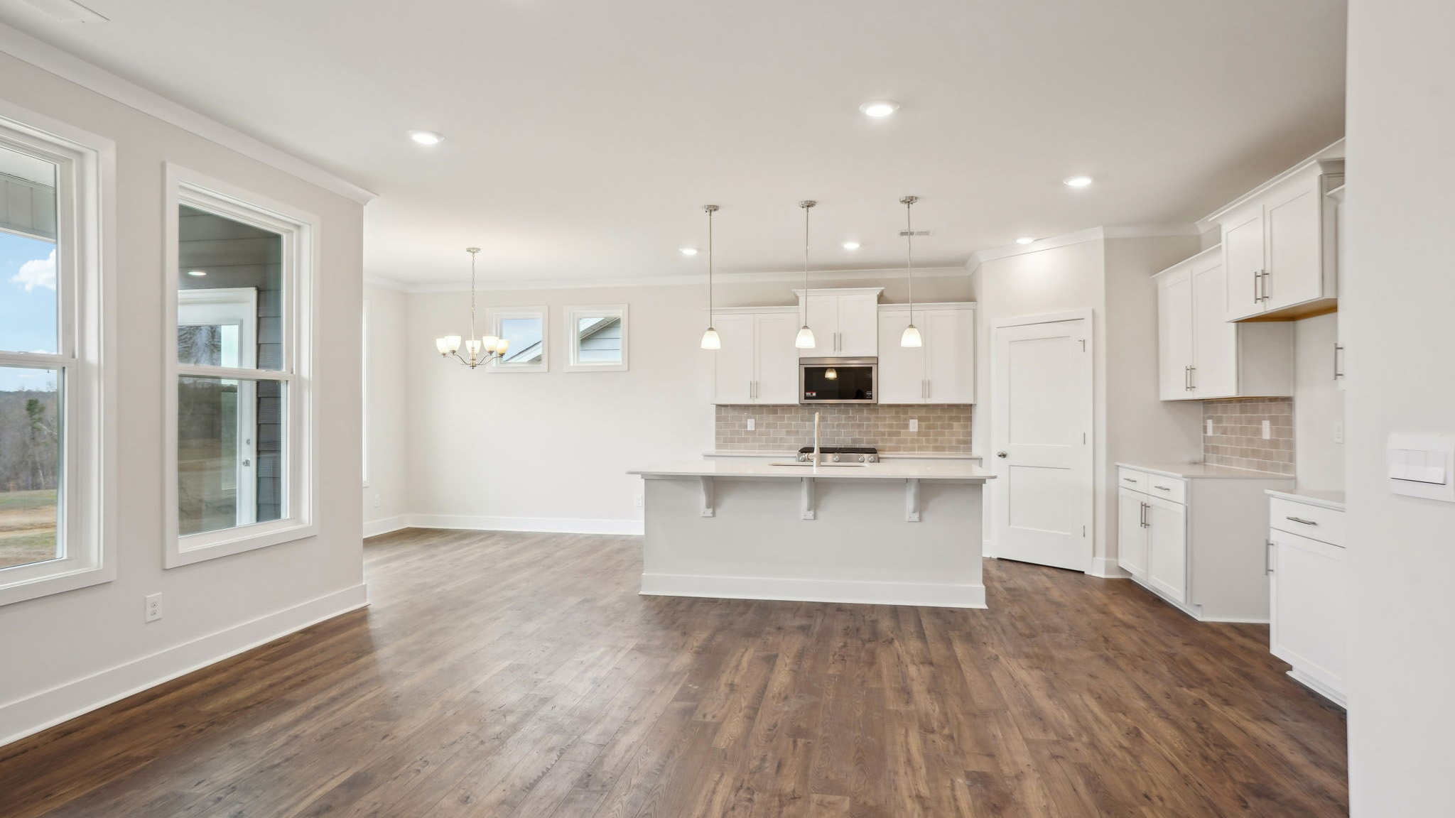 Kitchen and island with white cabinets, tile backsplash, quartz countertops, and stainless steel appliances