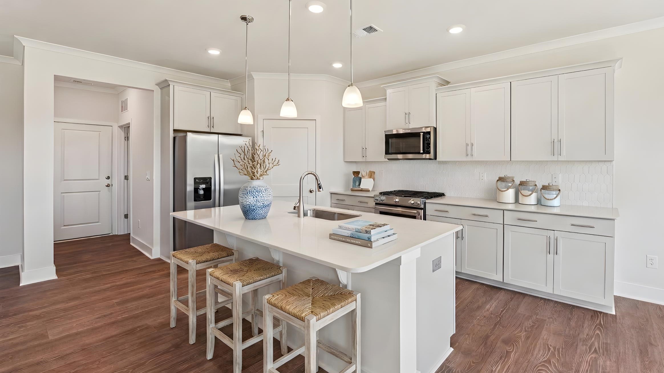 Kitchen and island with white cabinets, stainless steel appliances and hanging lights