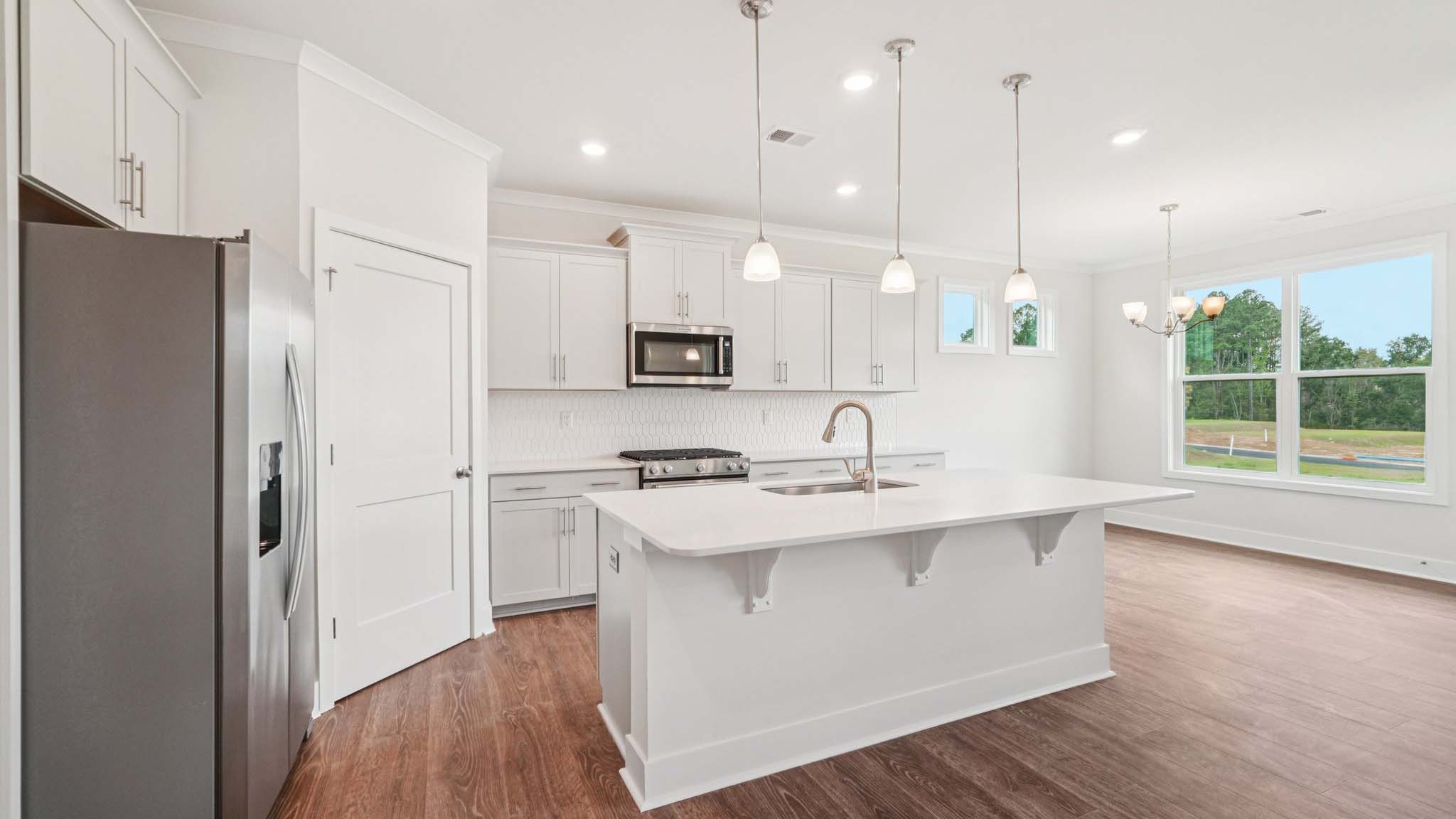 Kitchen and island with white cabinets, stainless steel appliances and hanging lights