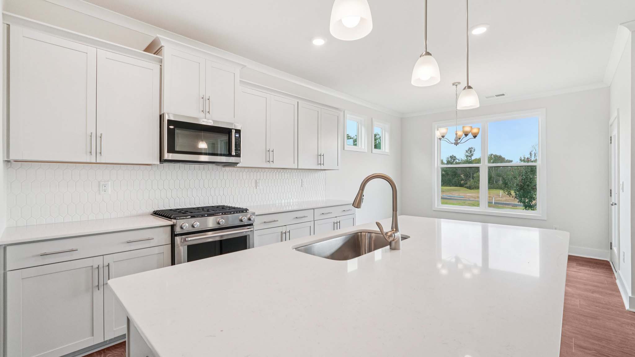 Kitchen and island with white cabinets, stainless steel appliances and hanging lights
