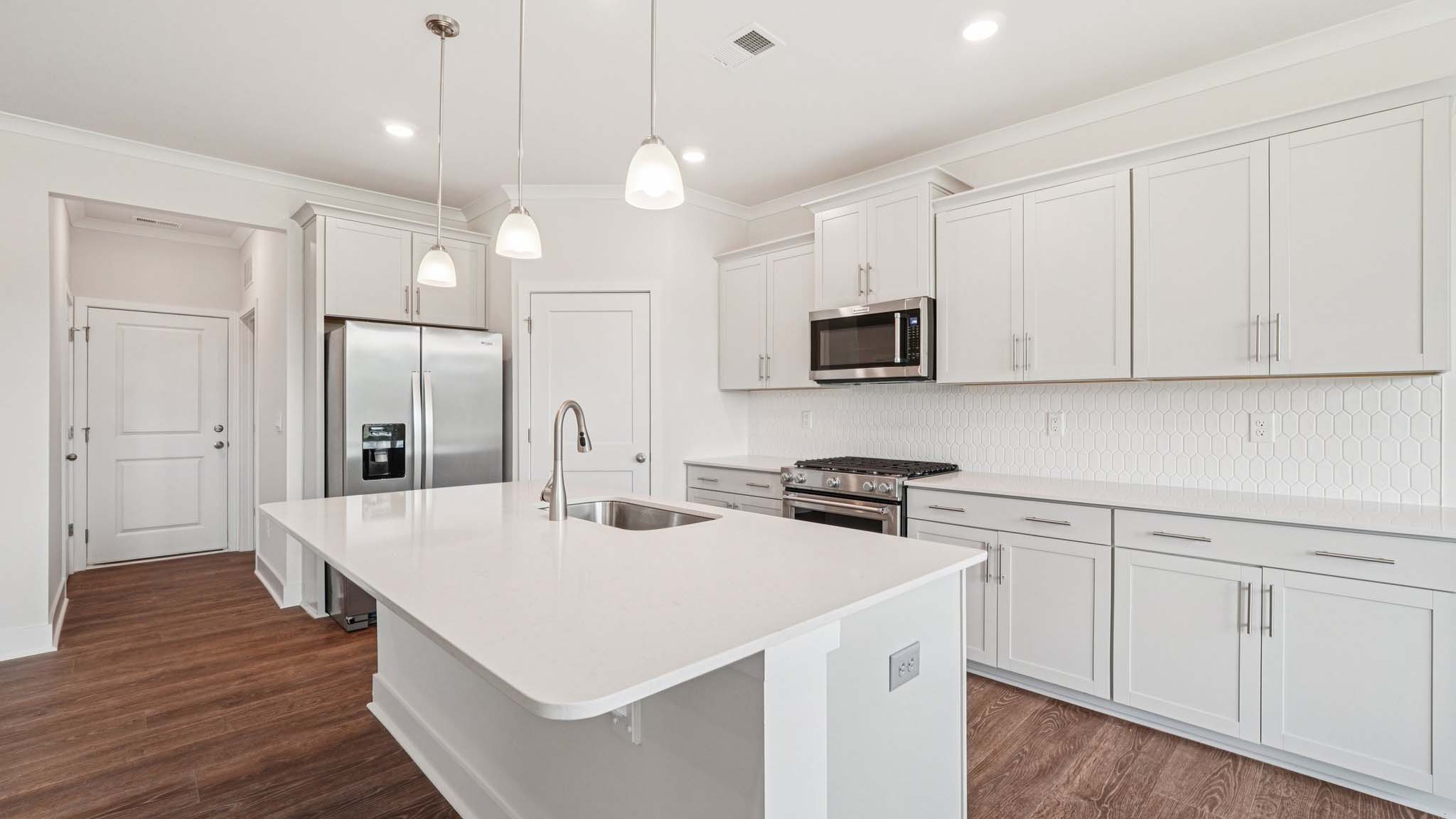 Kitchen and island with white cabinets, stainless steel appliances and hanging lights