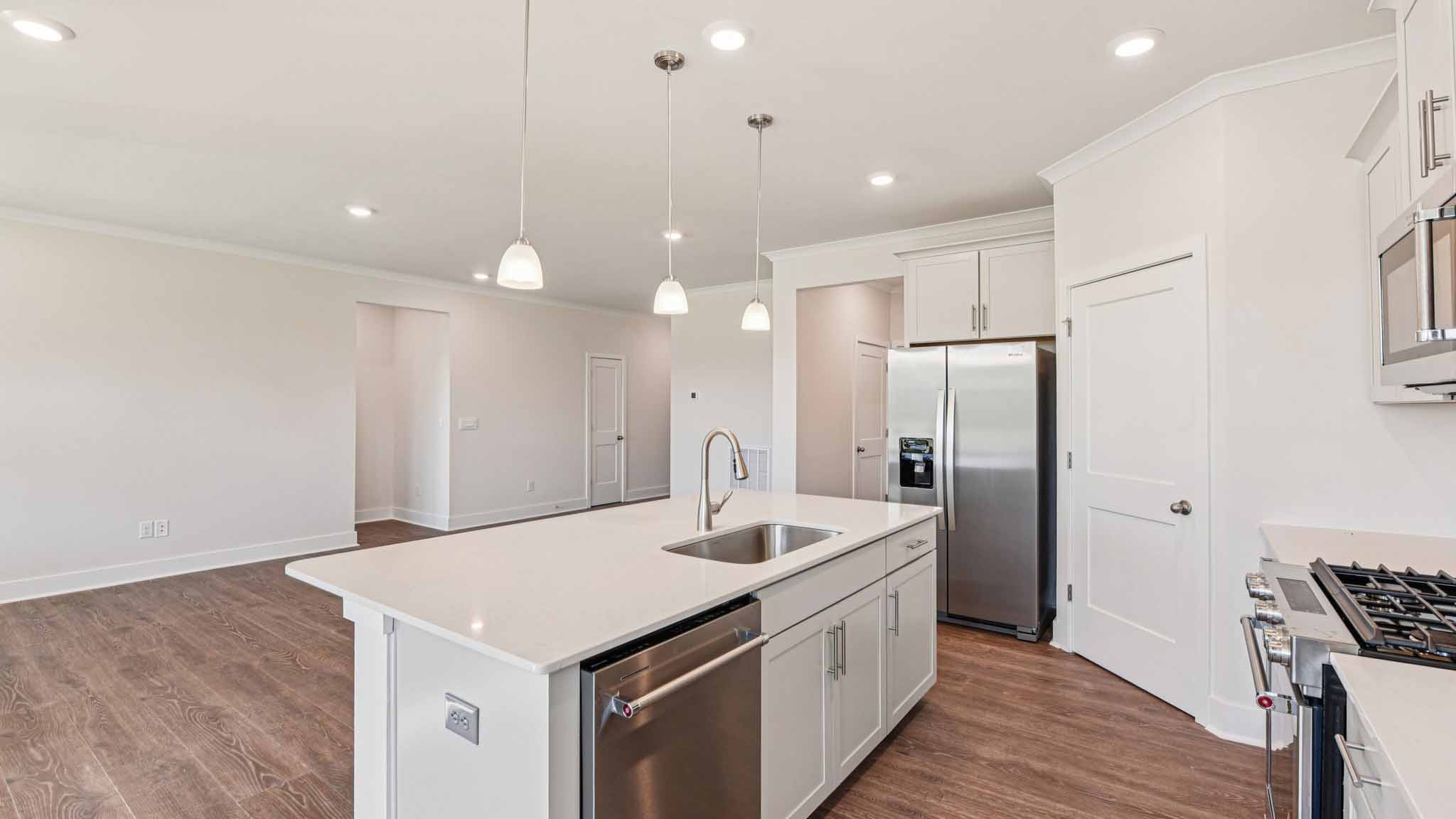 Kitchen and island with white cabinets, stainless steel appliances and hanging lights