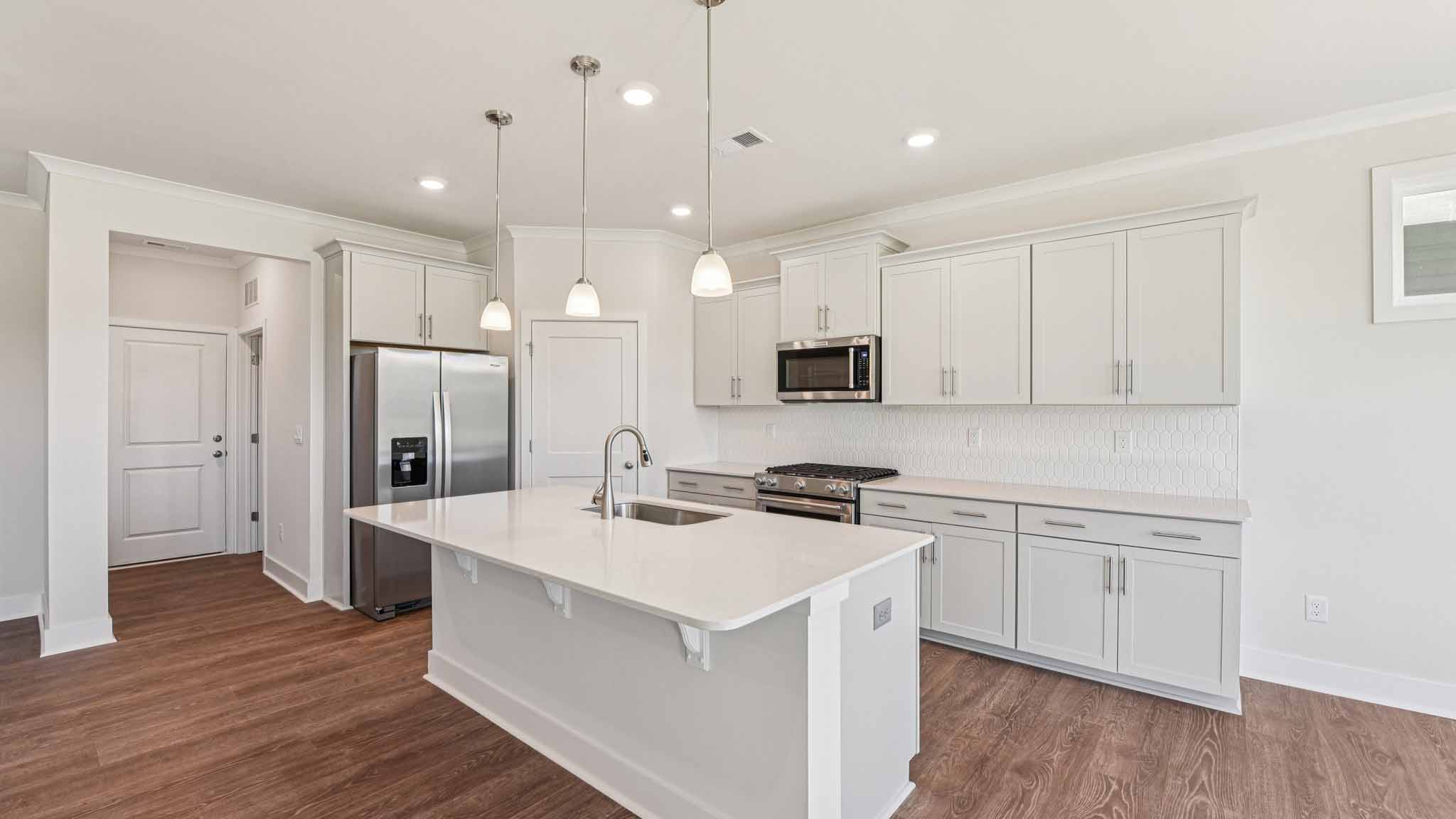 Kitchen and island with white cabinets, stainless steel appliances and hanging lights