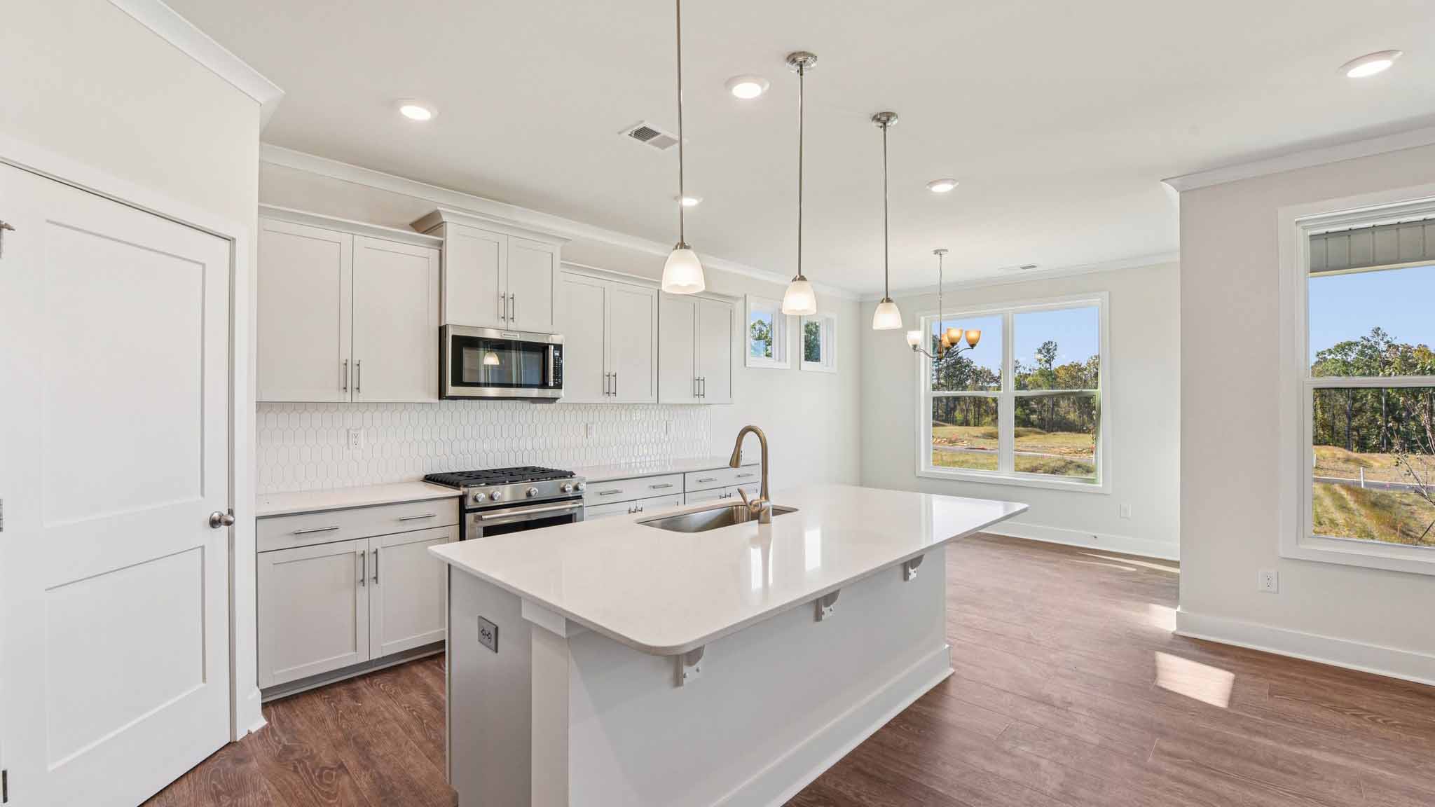Kitchen and island with white cabinets, stainless steel appliances and hanging lights