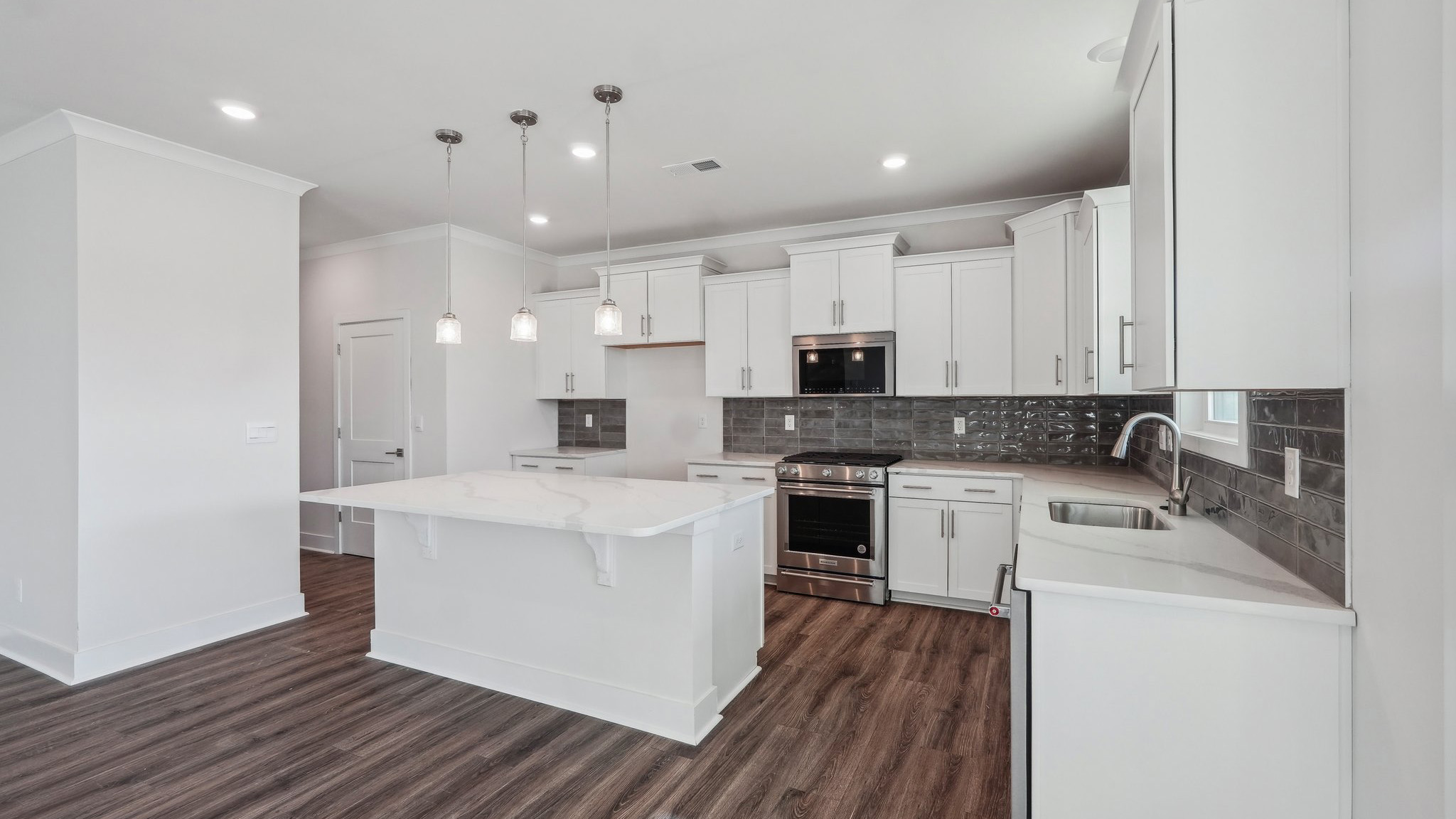 Kitchen and island with tile backsplash, white cabinets, and stainless steel backsplash