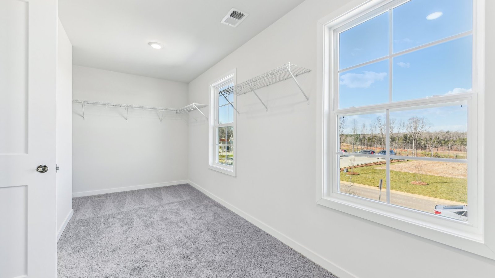 primary bedroom walk in closet carpeted with 2 large windows